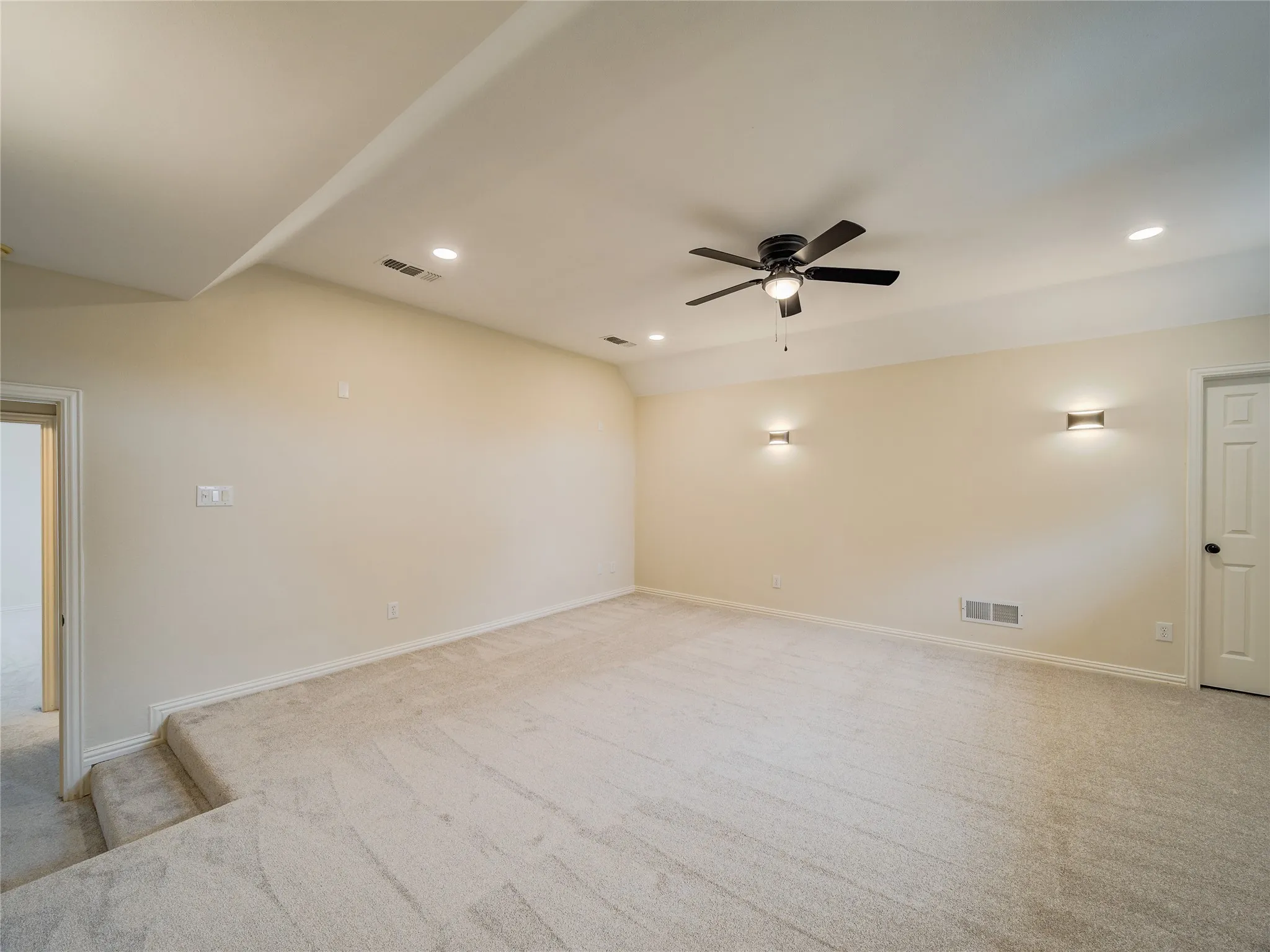 Spacious carpeted room featuring a ceiling fan, recessed lighting, and wall sconces