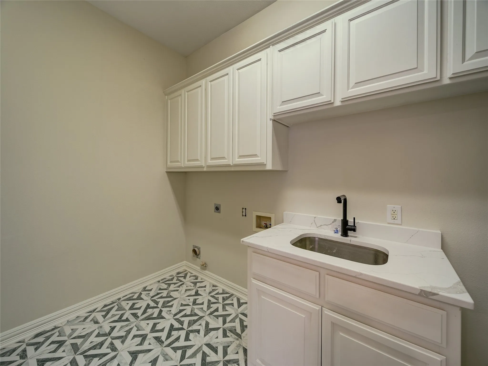 Laundry room featuring white shaker-style cabinetry, a white countertop with integrated sink, black faucet, and patterned floor tile