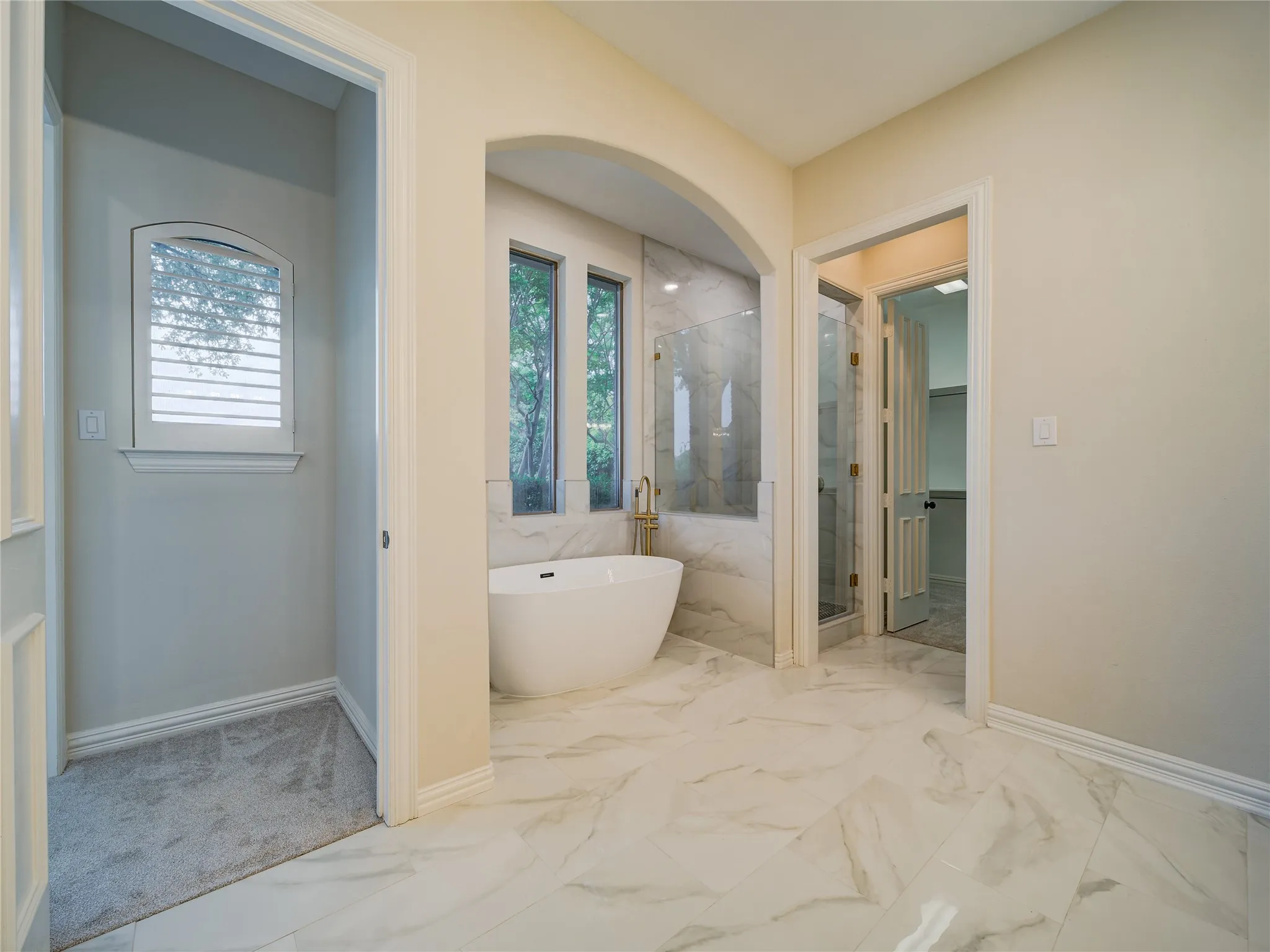 Freestanding soaking tub with gold-finish fixtures and surrounding marble-look wall tile