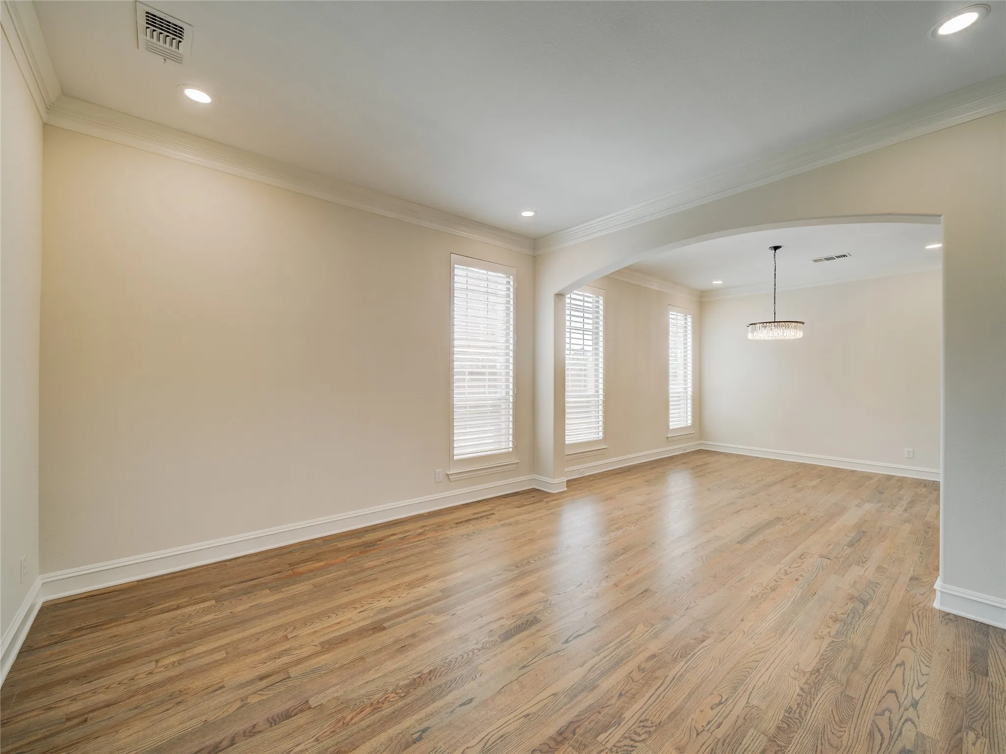 Spacious interior featuring wood-finish flooring, an arched doorway, and multiple windows with blinds