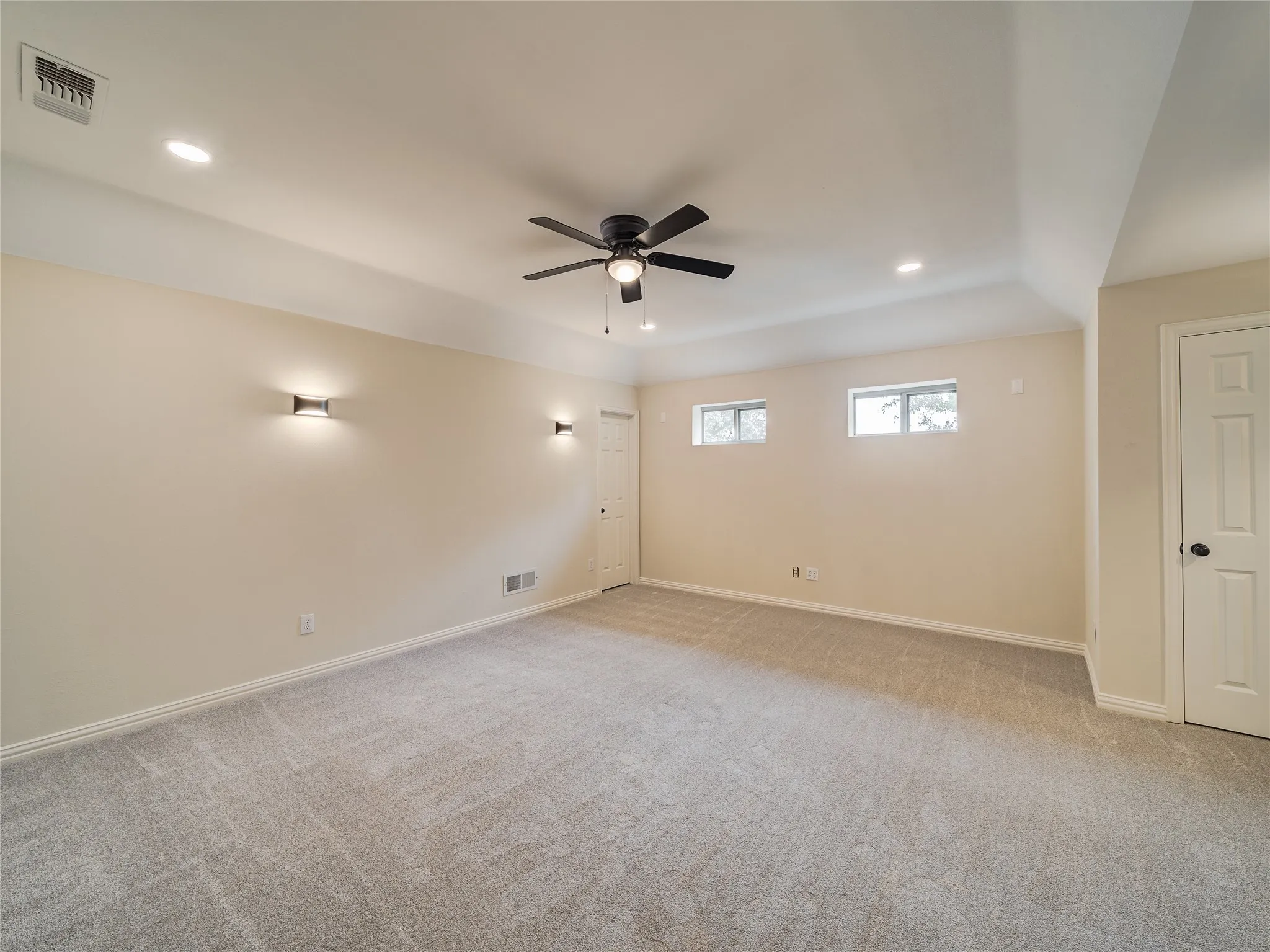 Spacious room featuring light gray carpeting, recessed lighting, a ceiling fan, and two windows