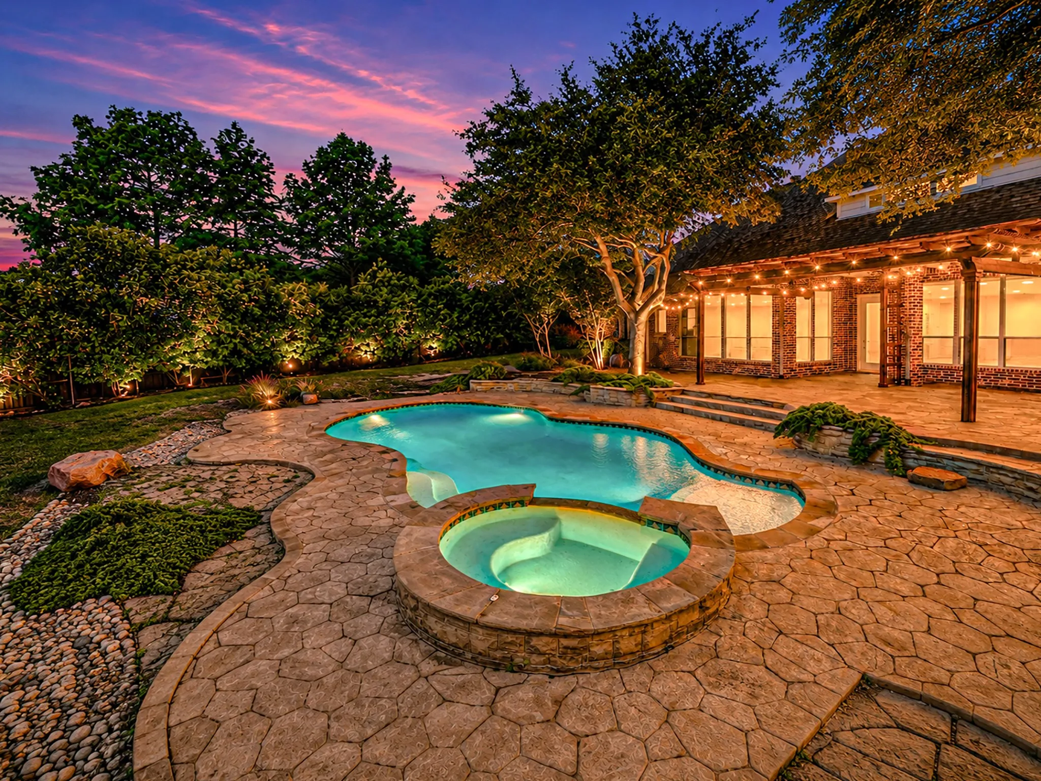 Brick exterior featuring a gabled roofline, decorative double entry doors, arched windows, manicured shrubs, and a concrete paver walkway
