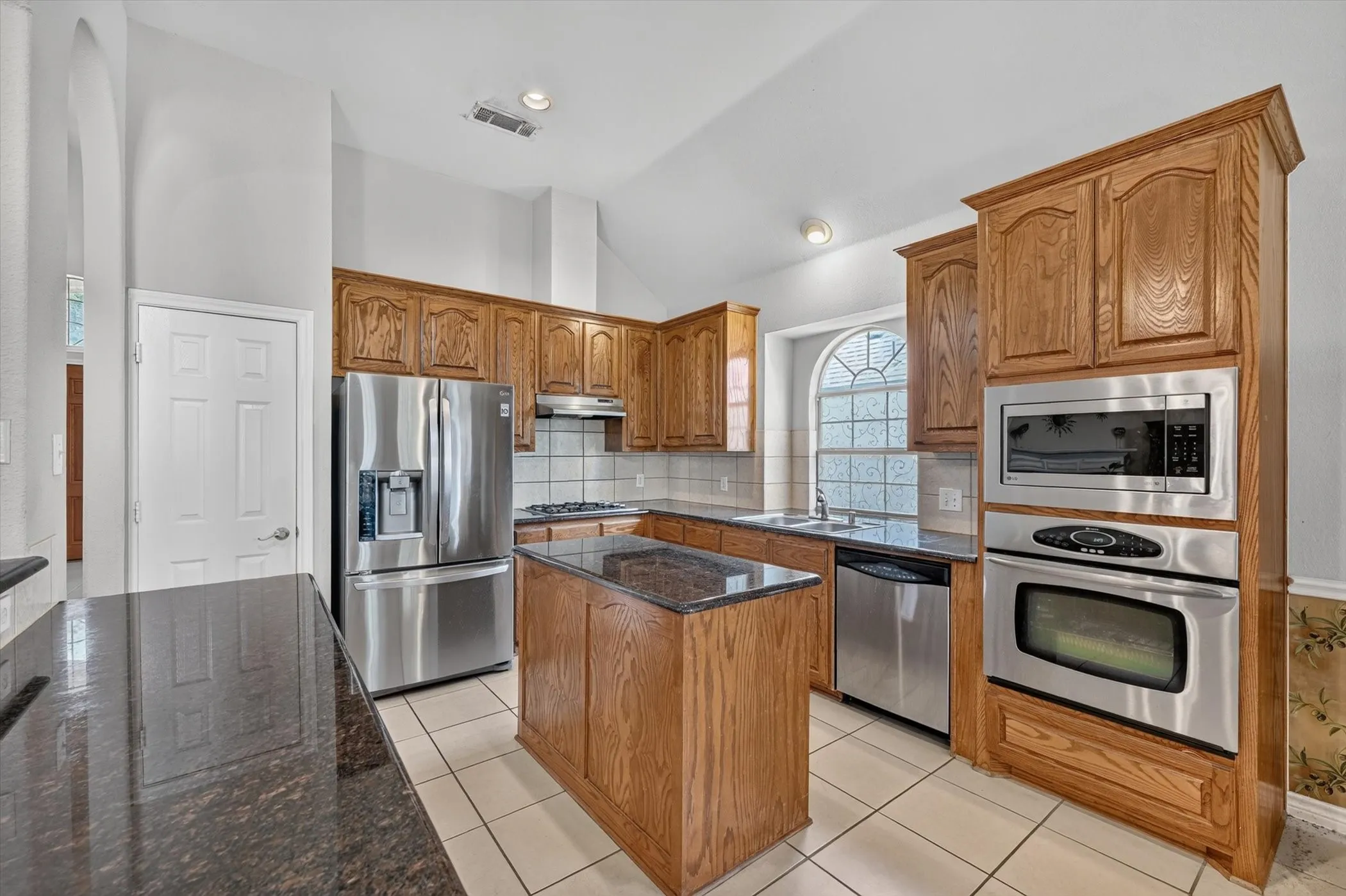 Kitchen featuring wood cabinetry, dark countertops, a stainless steel double sink, a gas cooktop, and a stainless steel refrigerator