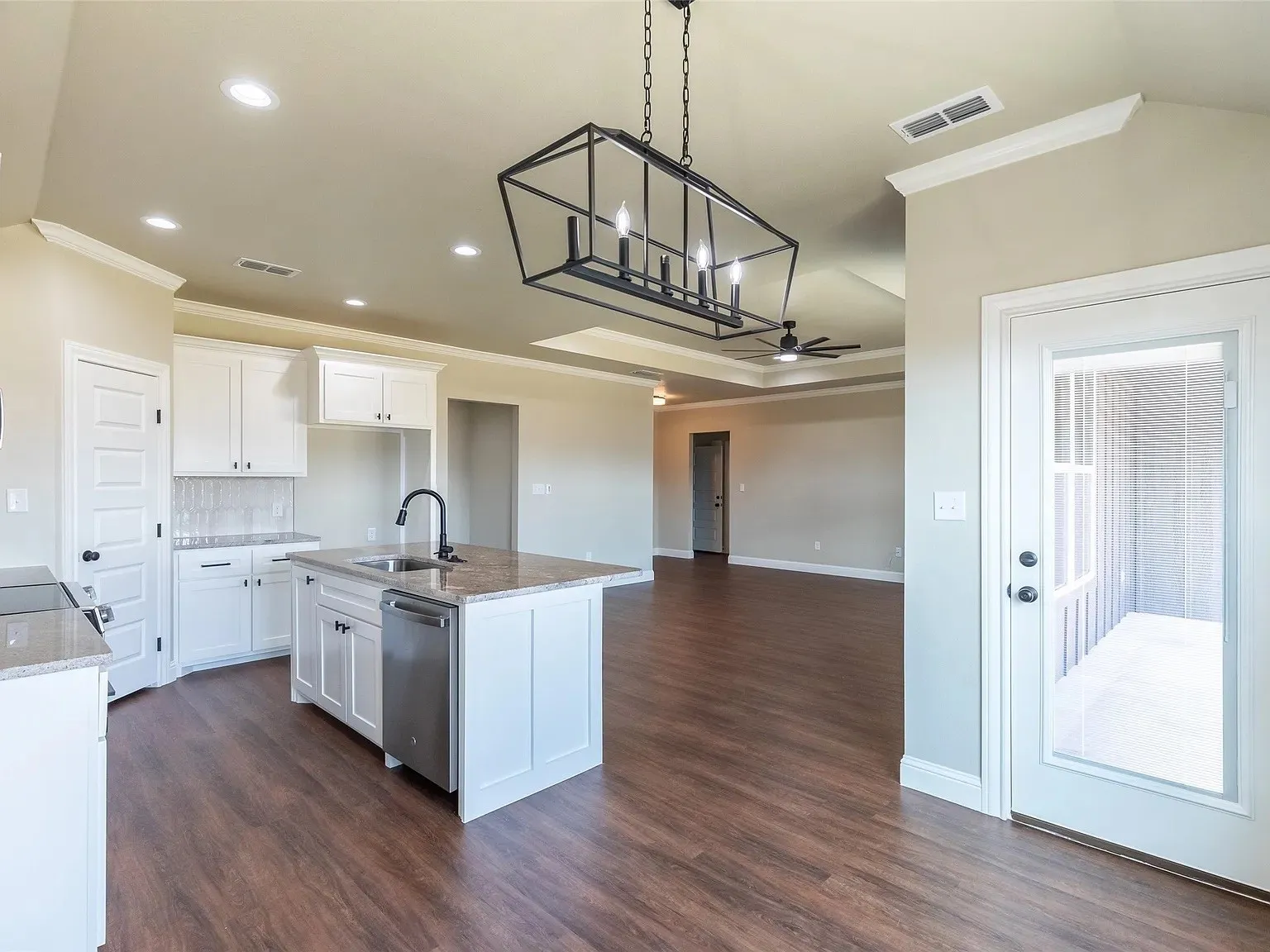 Open-concept kitchen featuring an island with sink and stainless steel dishwasher, white cabinetry, granite countertops, and a subway tile backsplash