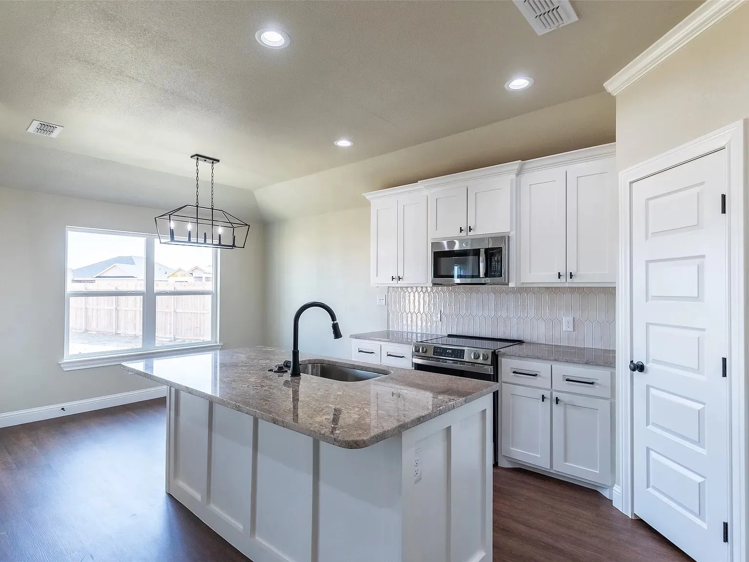 Kitchen featuring a central island with an undermount sink and granite-style countertop, white shaker-style cabinetry, stainless steel appliances, and wood-finish flooring