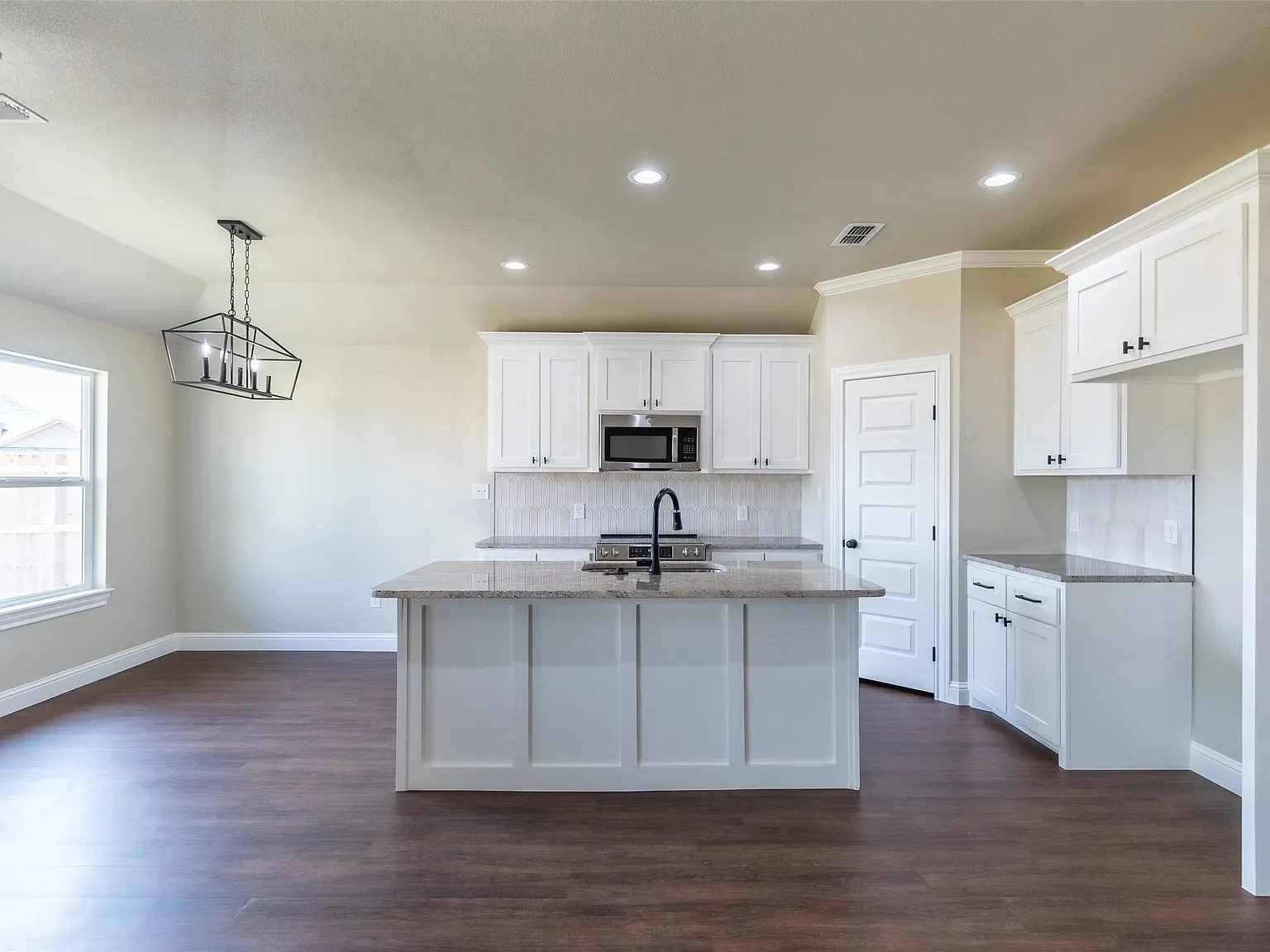 Kitchen featuring a central island with an undermount sink and matte black faucet, white shaker-style cabinetry, granite countertops, and a tiled backsplash