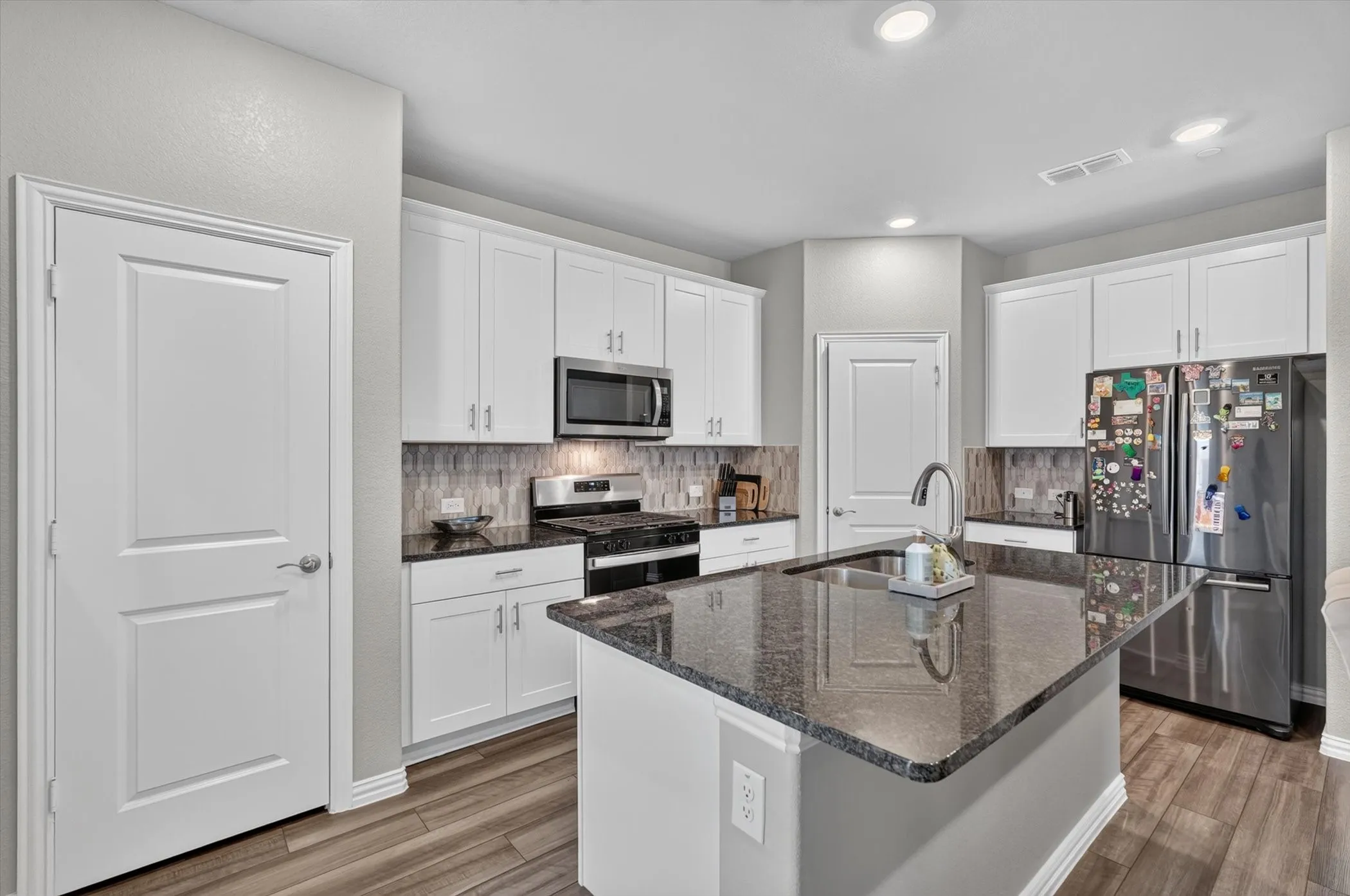 Kitchen featuring white cabinetry, dark stone countertops, wood-finish flooring, a stainless steel gas range, and a central island with an undermount sink