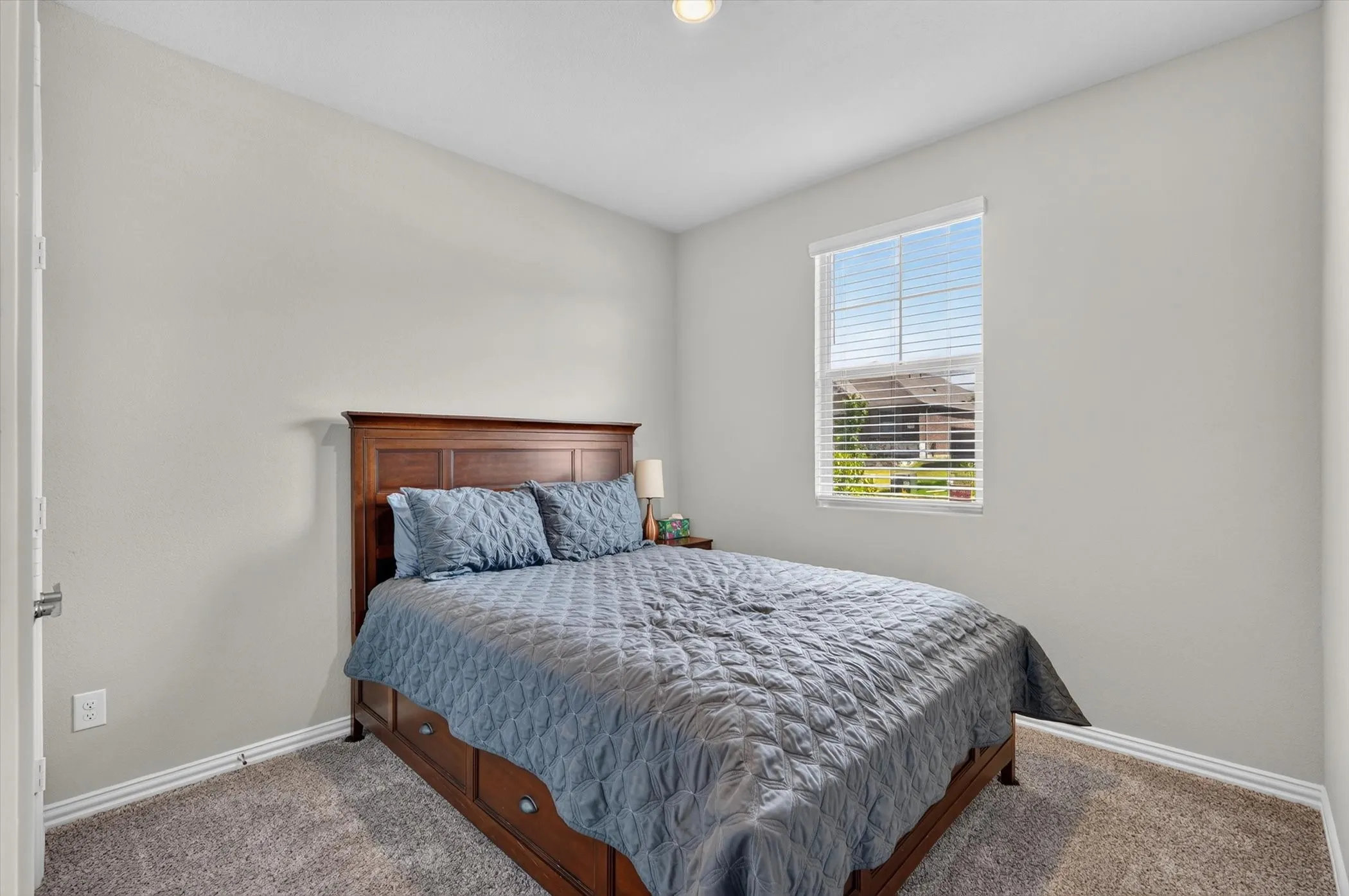 Carpeted bedroom featuring a single window with blinds, white baseboards, and neutral wall paint