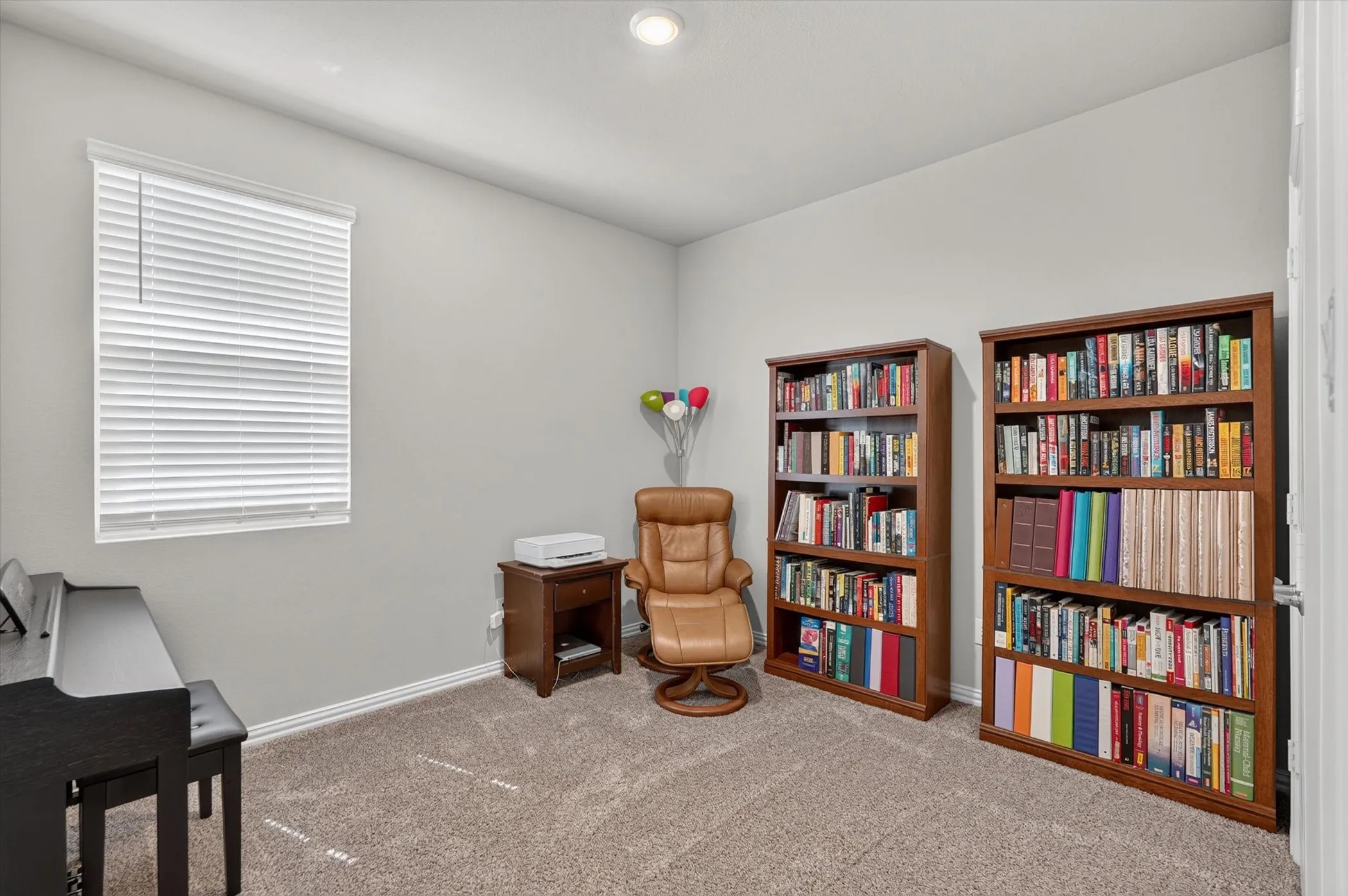 Carpeted interior room with white trim, recessed lighting, a window with blinds, and two built-in wood bookshelves