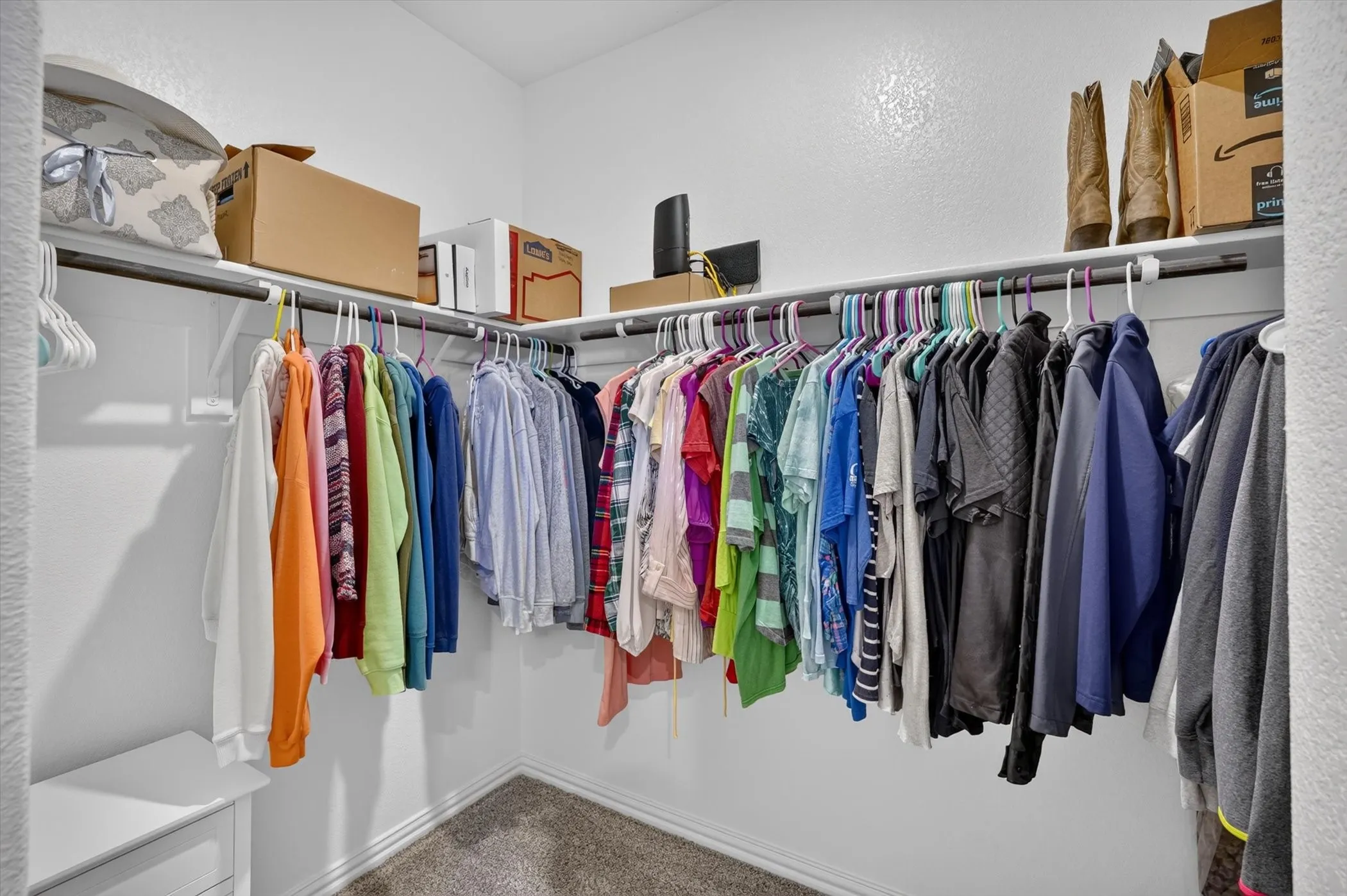 Walk-in closet featuring white walls, textured ceiling, wall-mounted shelving, hanging rods, and carpet flooring