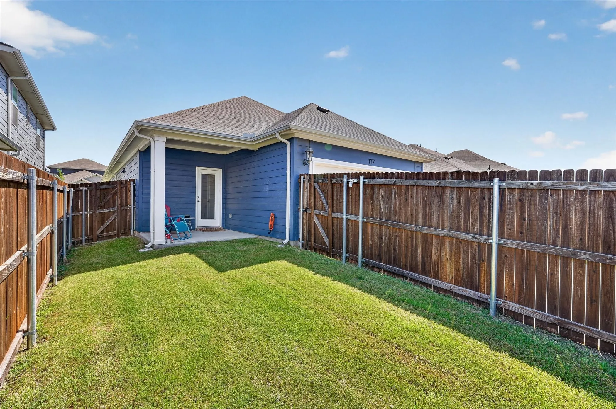 Expansive fenced backyard with a manicured lawn, featuring a covered patio and direct exterior access