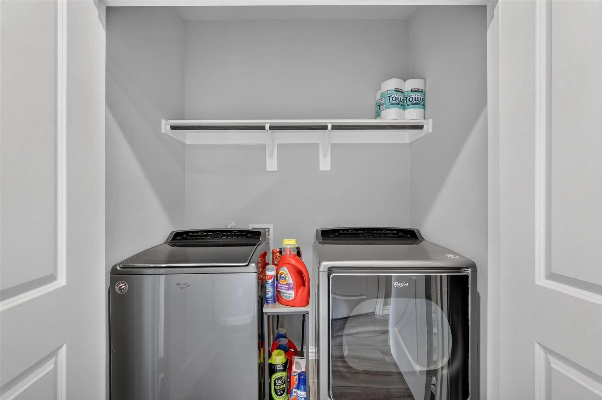 Dedicated laundry closet featuring a white wall shelf, light gray walls, and white trim