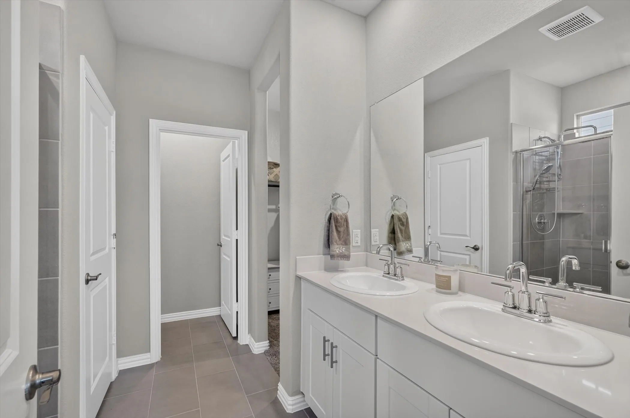 Contemporary bathroom featuring a dual vanity with white cabinetry and chrome fixtures, a full-width mirror, and a glass-enclosed shower with subway tile