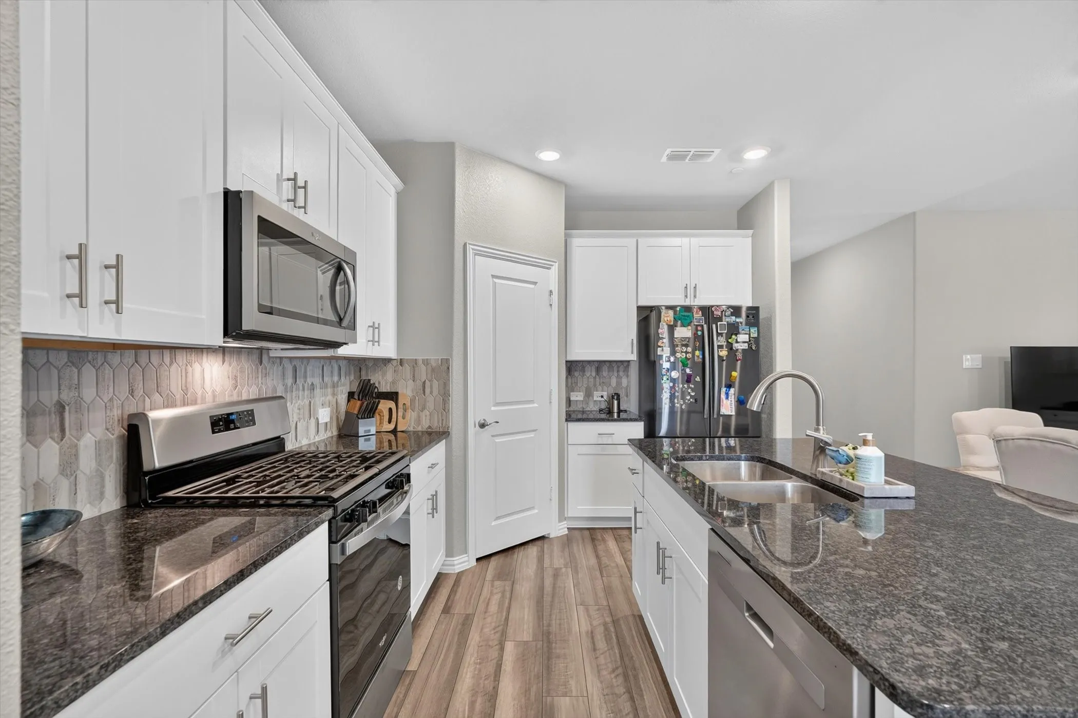 Modern kitchen featuring white cabinetry, dark speckled countertops, and stainless steel appliances