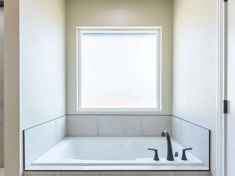 Built-in soaking tub featuring matte black fixtures, integrated tile surround, and an opaque privacy window