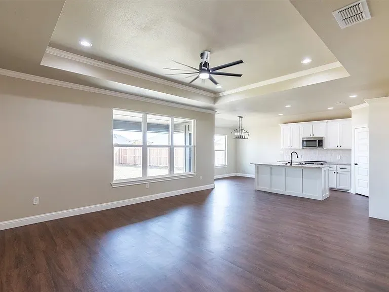 Open-concept living space featuring wood-finish flooring, a tray ceiling with recessed lighting and a ceiling fan, and large windows