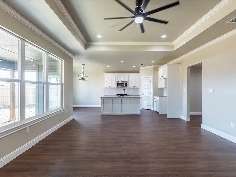 Open-concept living space featuring wood-finish flooring, large windows, and a tray ceiling with recessed lighting and a ceiling fan