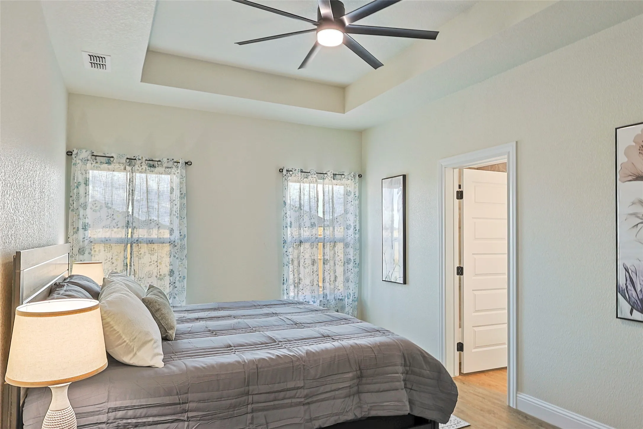 Tray ceiling with a modern ceiling fan, paired with multiple windows featuring decorative curtains