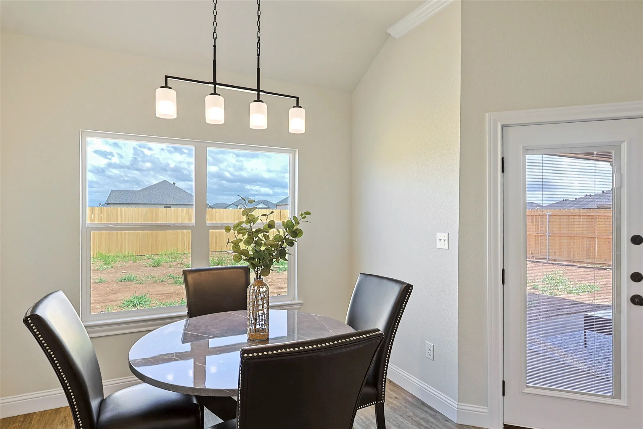 Spacious dining area featuring a four-light linear chandelier, vaulted ceiling, and a large window