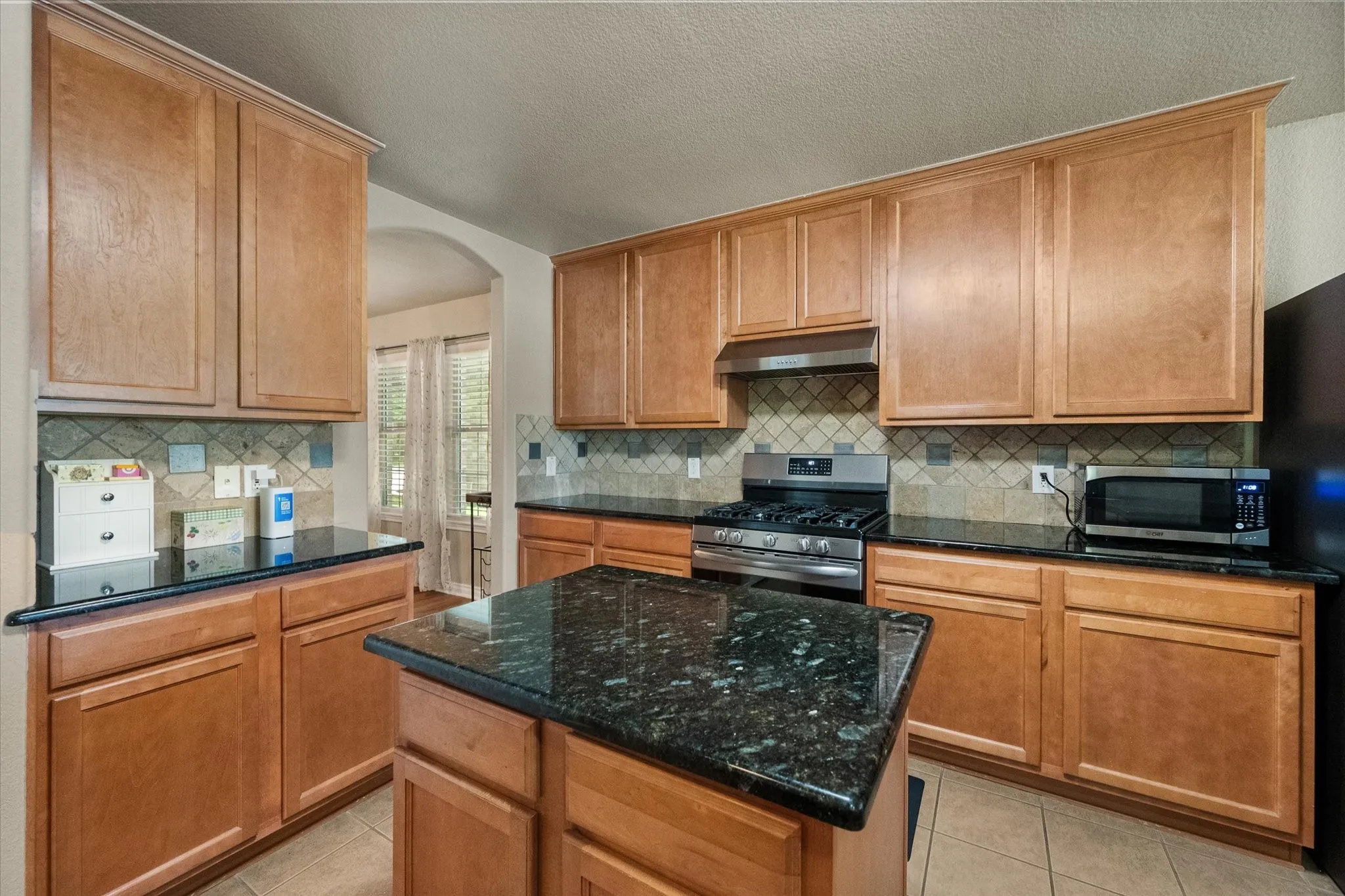 This beautifully appointed kitchen combines style, functionality, and abundant storage, making it the heart of the home. Featuring rich wood cabinetry, sleek granite countertops, a spacious center island, and a recently updated gas range, this kitchen is designed for both everyday living and effortless entertaining. The timeless tile backsplash and durable tile flooring add warmth and character, while expansive counter space provides plenty of room for meal preparation. A large walk-in pantry and extensive cabinetry offer exceptional storage for cookware, small appliances, and pantry essentials, keeping everything organized and within reach. Open to the main living areas, this inviting kitchen delivers the perfect blend of comfort, convenience, and modern appeal.