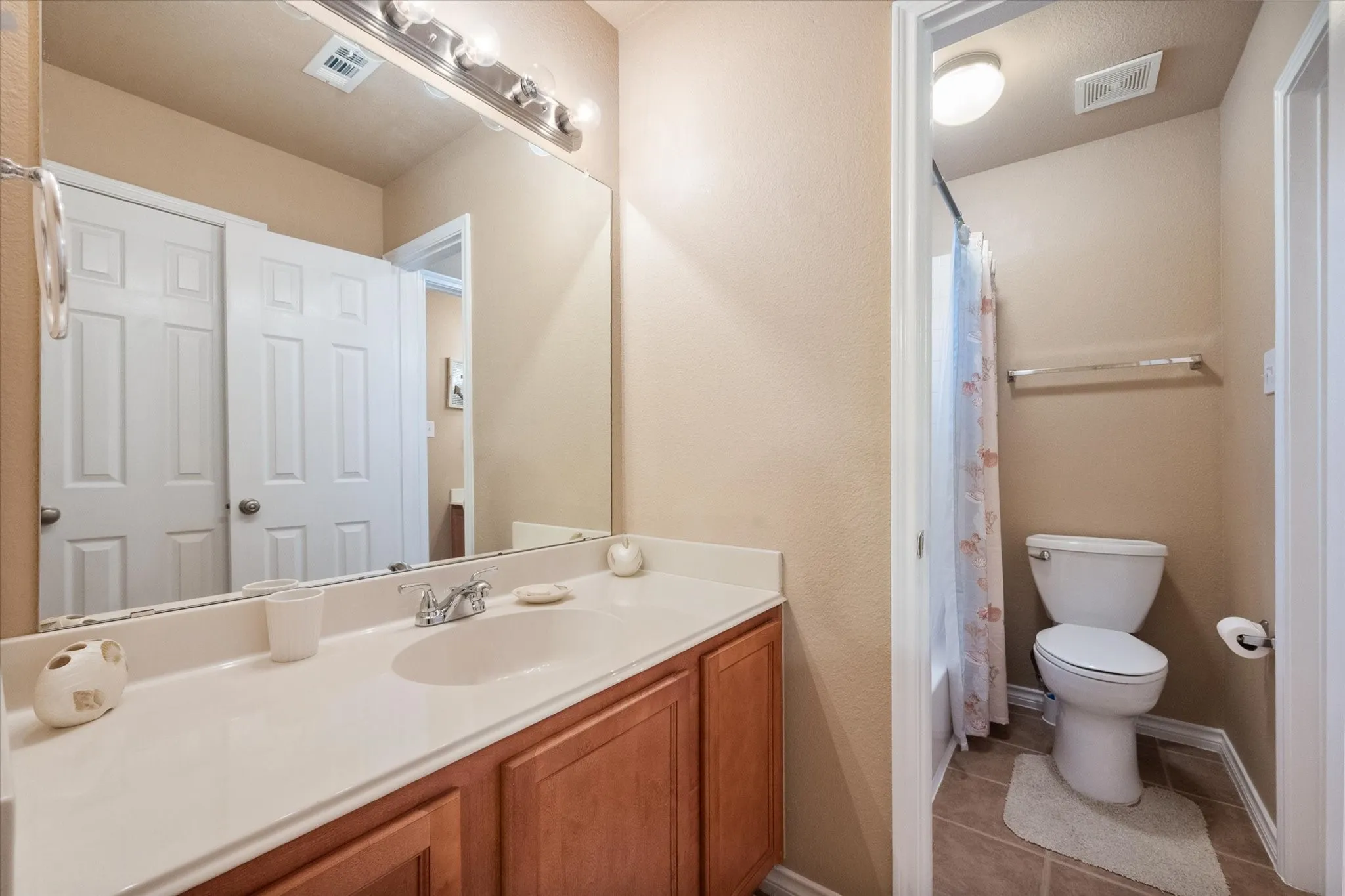 This upstairs full bathroom is thoughtfully designed with a spacious single-sink vanity, extended countertop, and a tub/shower combination for everyday convenience. Warm wood cabinetry, a large wall mirror, and bright vanity lighting create a clean, functional space with ample room for storage and daily routines. Conveniently located upstairs to serve the secondary bedrooms, this well-maintained bathroom offers comfort, practicality, and move-in-ready appeal for family members and overnight guests.