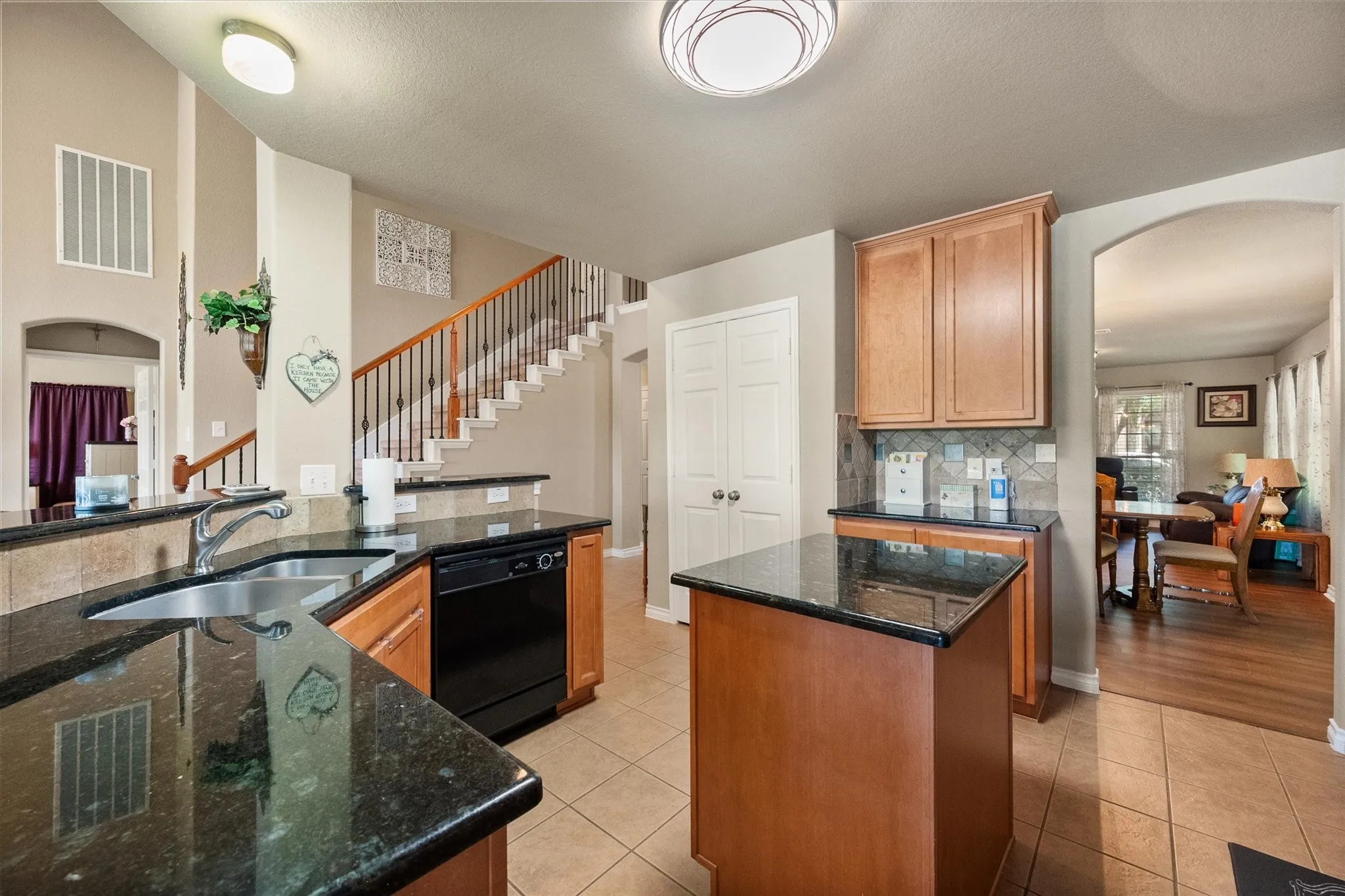 Designed with both style and functionality in mind, this spacious kitchen offers an exceptional workspace for home chefs and everyday living. The efficient layout features expansive granite countertops, a center island for additional prep space, abundant wood cabinetry for storage, and a double-basin sink with views into the main living area. Black appliances, a tile backsplash, and durable tile flooring add timeless appeal, while the open-concept design keeps you connected to family and guests. A large pantry provides even more storage, making organization effortless. With generous counter space, multiple work zones, and seamless flow to the dining and living areas, this kitchen is ideal for meal preparation, entertaining, and busy households.**SEO Keywords Included:** kitchen workspace, granite countertops, center island, spacious kitchen, abundant cabinetry, pantry, open-concept kitchen, meal prep, functional layout, double sink, tile flooring, entertaining kit
