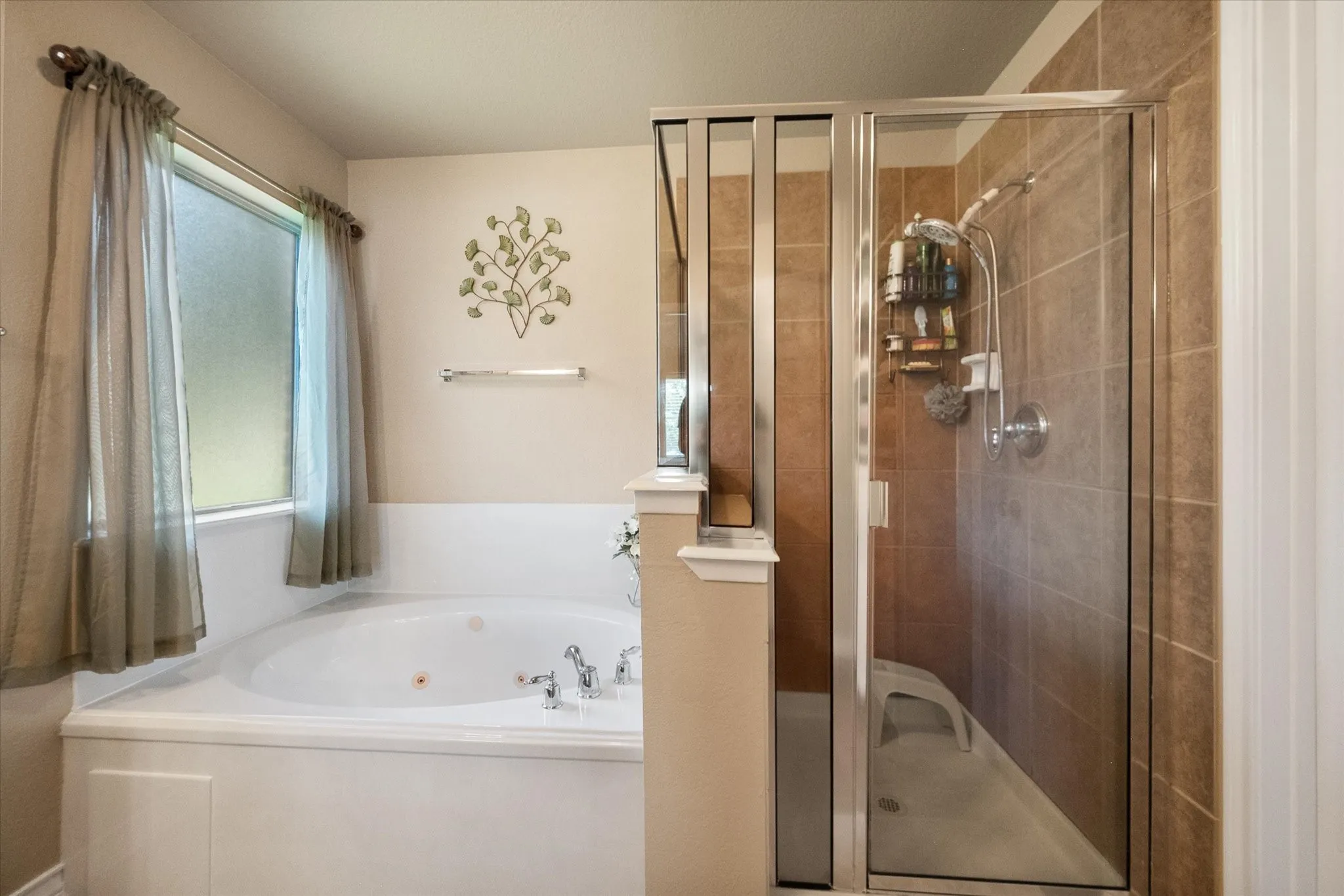 Enjoy a spa-like experience in the luxurious primary bathroom, showcasing a relaxing soaking tub paired with a separate glass-enclosed walk-in shower. This thoughtfully designed ensuite features elegant tile surrounds, abundant natural light, and a spacious layout that creates the perfect setting for relaxation and everyday comfort. Whether enjoying a peaceful soak or a refreshing shower, this well-appointed primary bath offers both style and functionality.