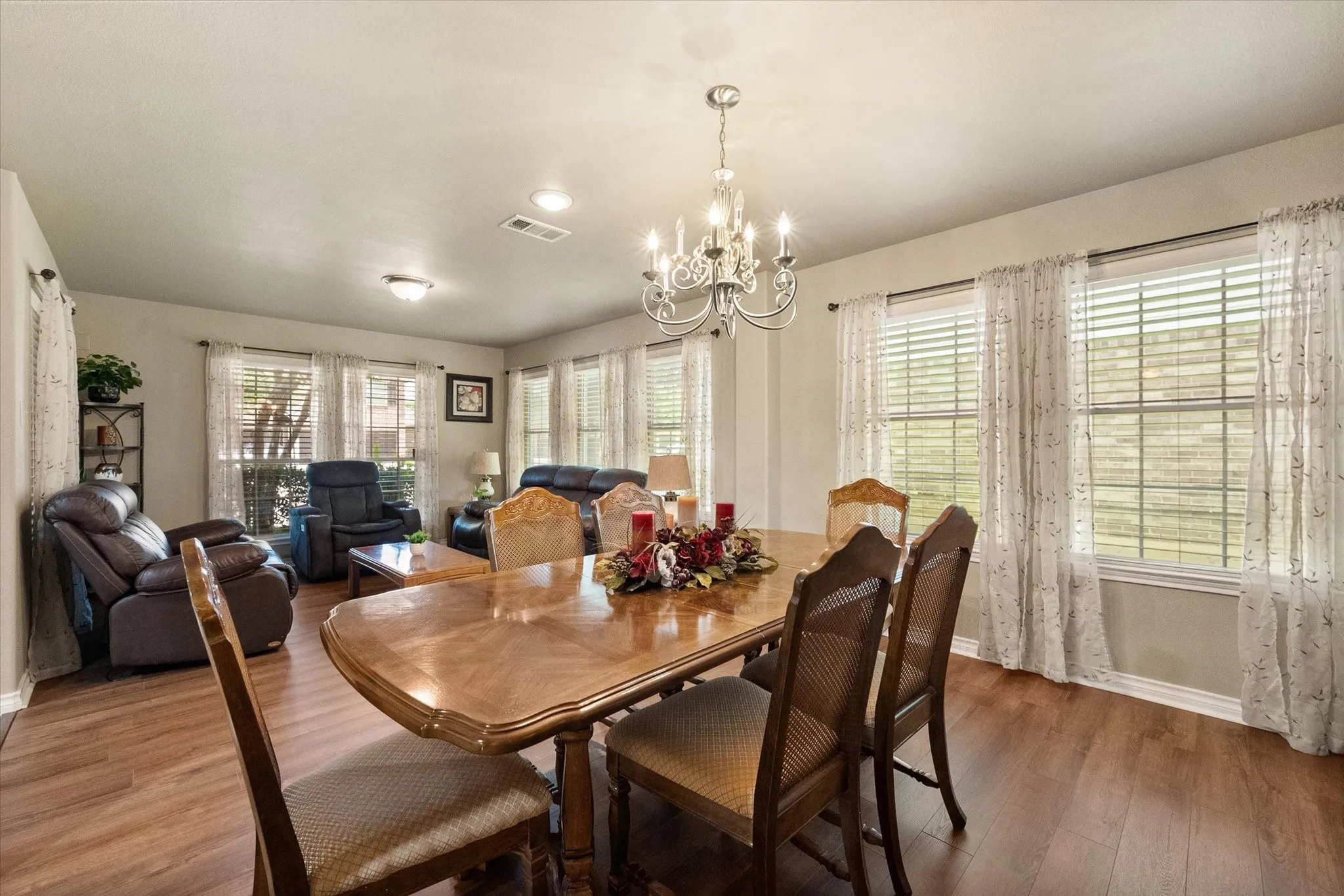 Elegant formal living and formal dining rooms welcome you with an abundance of natural light streaming through walls of oversized windows. The open-concept layout offers the perfect setting for entertaining guests, hosting holiday dinners, or everyday gatherings. Rich wood-look flooring, neutral designer colors, and an elegant chandelier create a warm, inviting atmosphere that complements any décor style. The spacious formal dining area easily accommodates a large dining table, while the adjacent formal living room provides a comfortable space for conversation and relaxation. Located at the front of the home, these versatile spaces showcase the home's bright, airy feel and seamless flow, making this Mira Lagos home ideal for both casual living and formal entertaining.