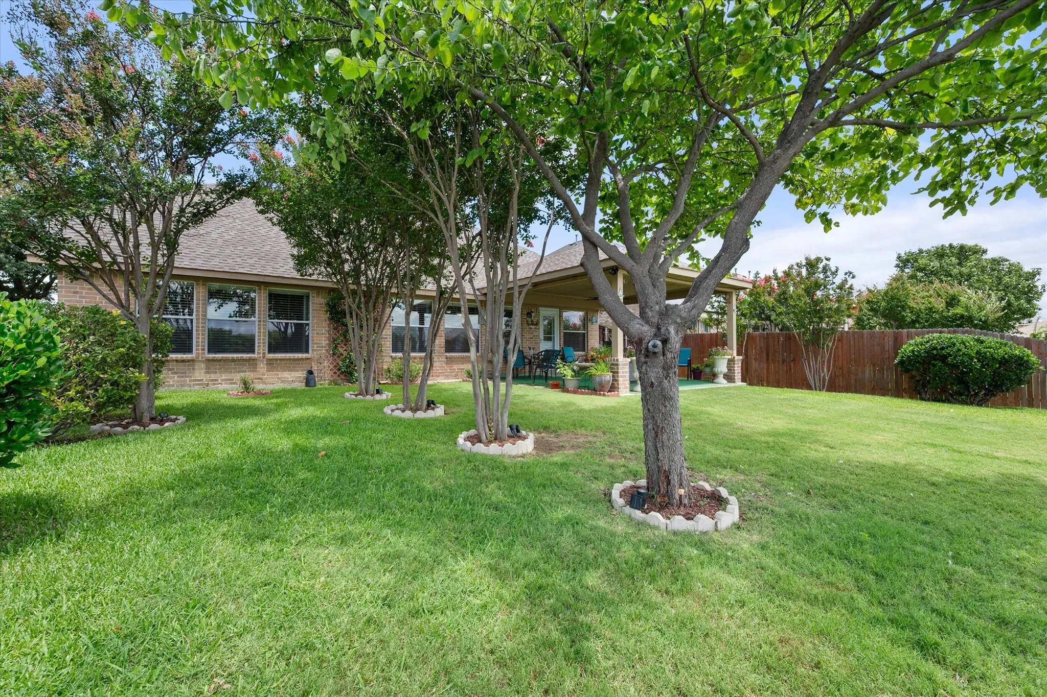 Escape to your own private backyard oasis featuring mature shade trees, lush St. Augustine grass, and professionally maintained landscaping. The expansive yard is equipped with a full sprinkler system, keeping the lawn vibrant and green year-round. An oversized covered patio with a ceiling fan creates the perfect space for outdoor dining, entertaining, or relaxing in the shade. The spacious fully fenced backyard offers plenty of room for children, pets, gardening, or future outdoor amenities while providing privacy and comfort. This beautifully maintained outdoor living space combines exceptional curb appeal, functionality, and the sought-after features today's homebuyers are searching for, including a large backyard, covered patio, mature trees, St. Augustine lawn, and automatic sprinkler system.