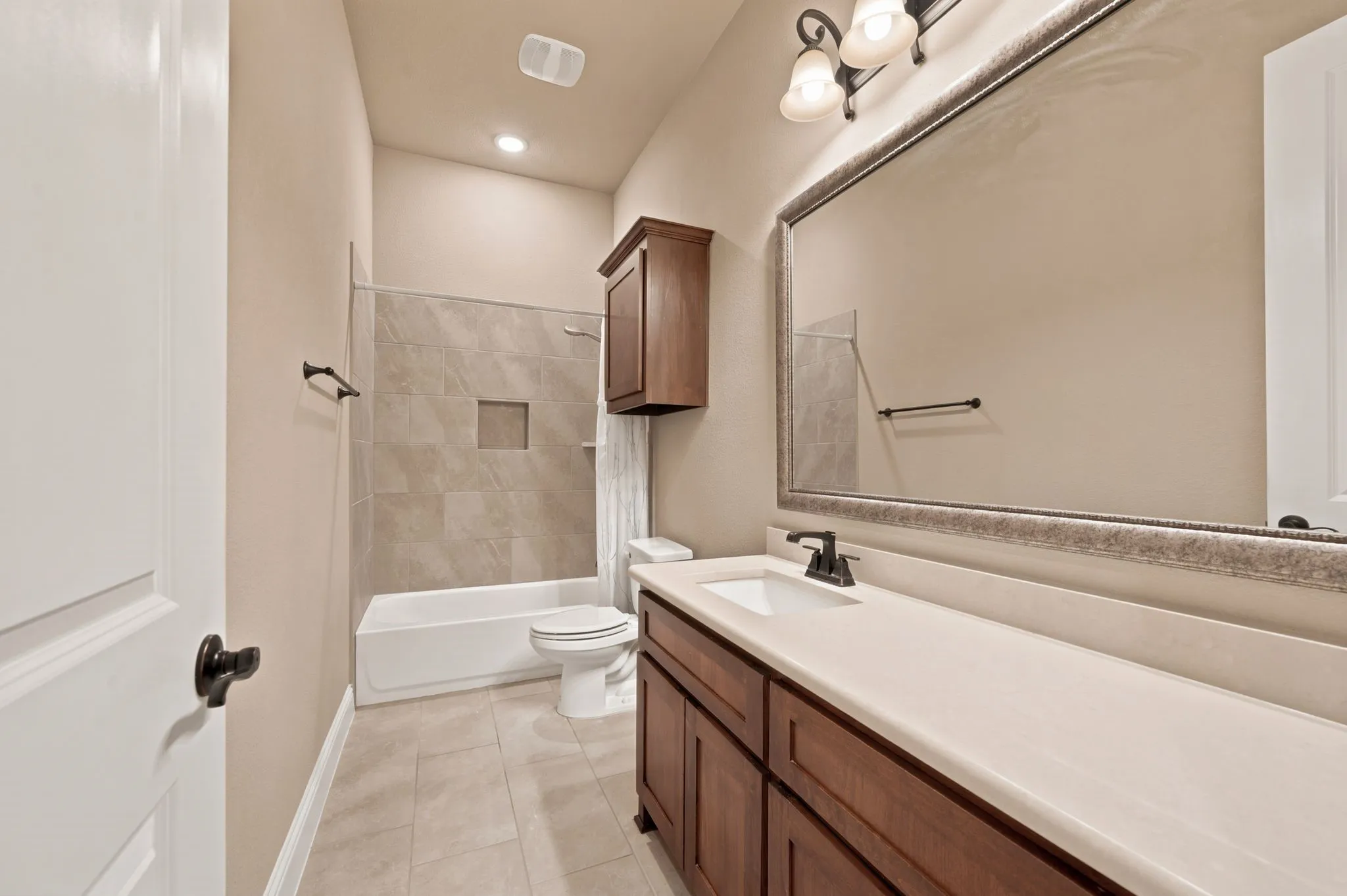 Secondary bathroom with ample counter space, framed mirror, bronze fixtures, Linen cabinet and tile surround tub-shower. Tile flooring.