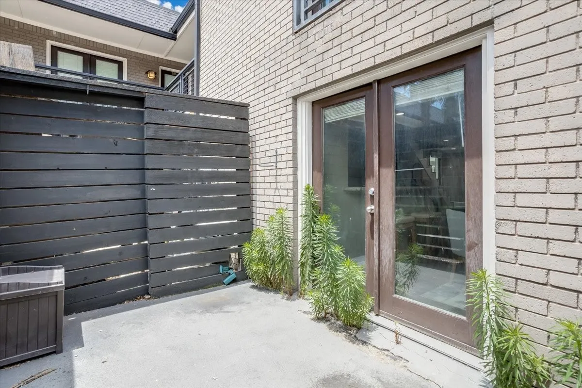 Private patio space featuring a neutral concrete surface, a dark-stained horizontal slat fence, and light-colored brick exterior