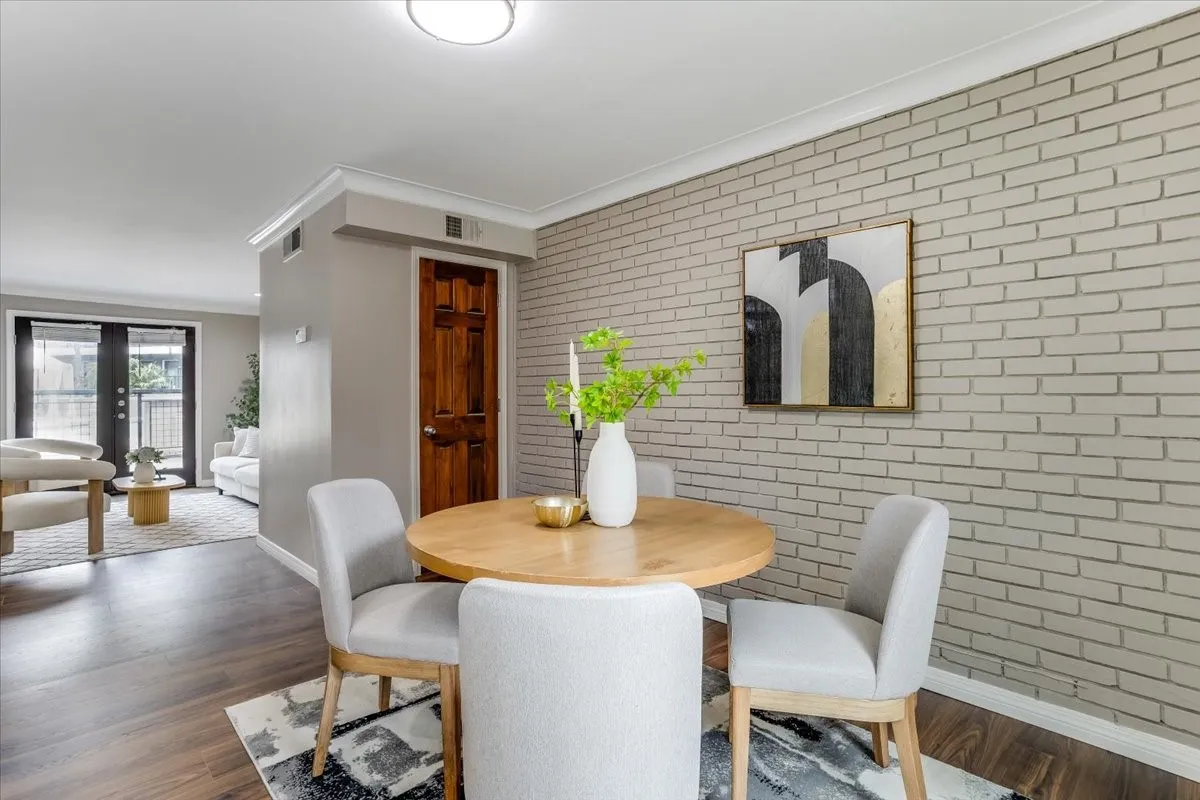 Dining area featuring a wood-finish round table and upholstered chairs, complemented by an accent brick-patterned wall