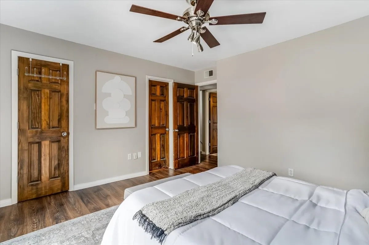 Bedroom featuring wood-finish flooring, light gray walls, a ceiling fan with wood blades and brushed nickel accents, and multiple paneled wood doors