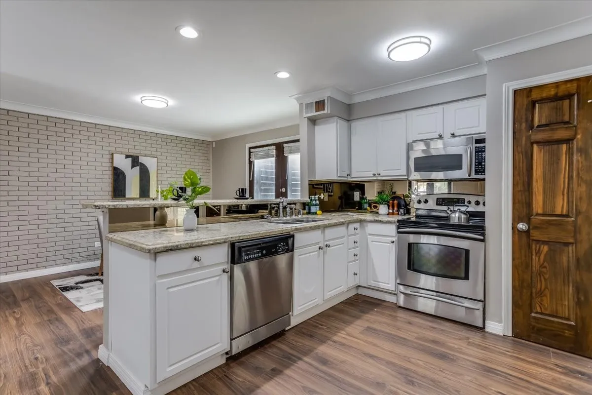 Kitchen featuring wood-finish flooring, white cabinetry, granite countertops, and stainless steel appliances