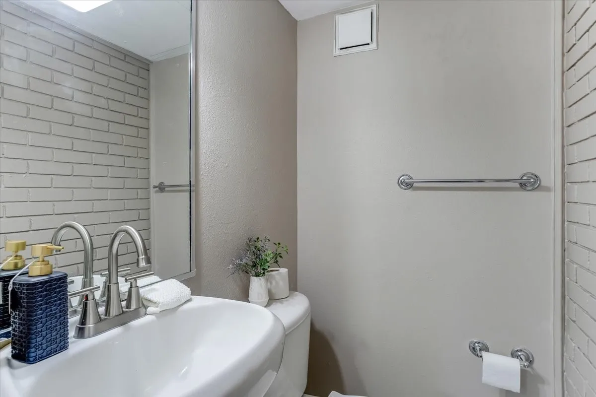 Pedestal sink with dual-handle faucet, chrome hardware, full-height mirror, and light-toned brick-patterned wall covering