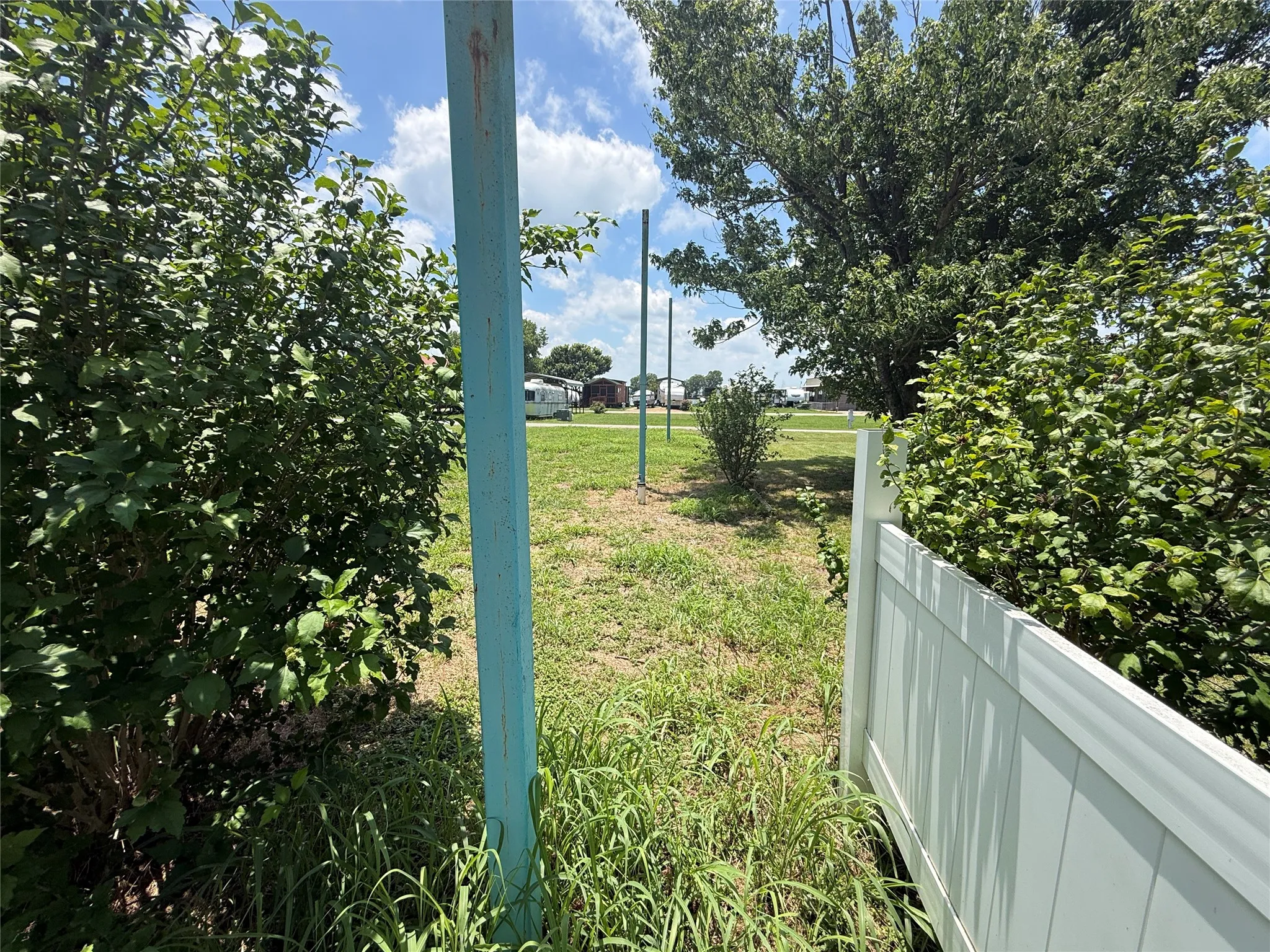 Side yard access view with fencing, 3 poles in place for future covered parking, and open grass area.