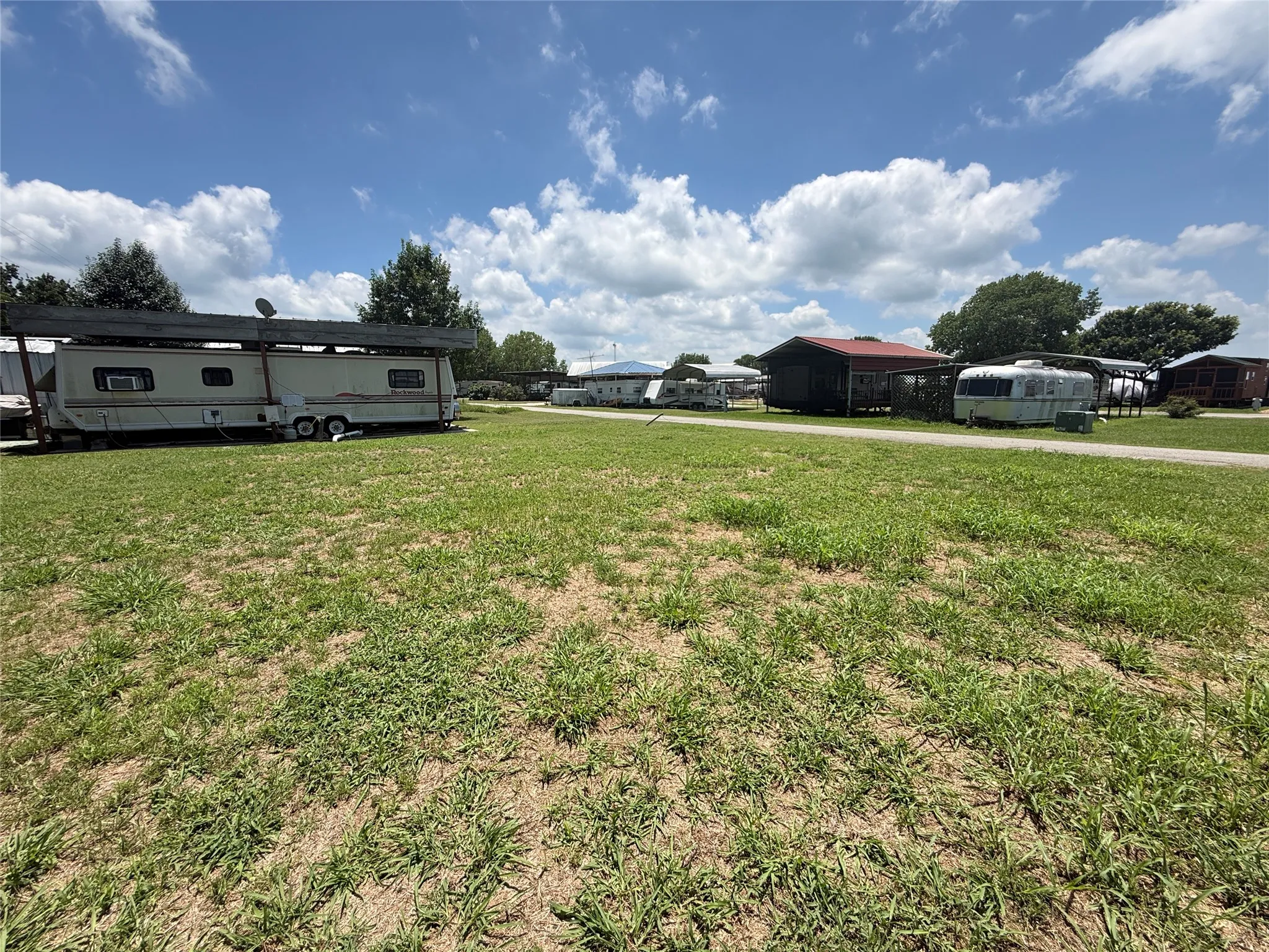 Open grassy area with two storage buildings and mature trees nearby.