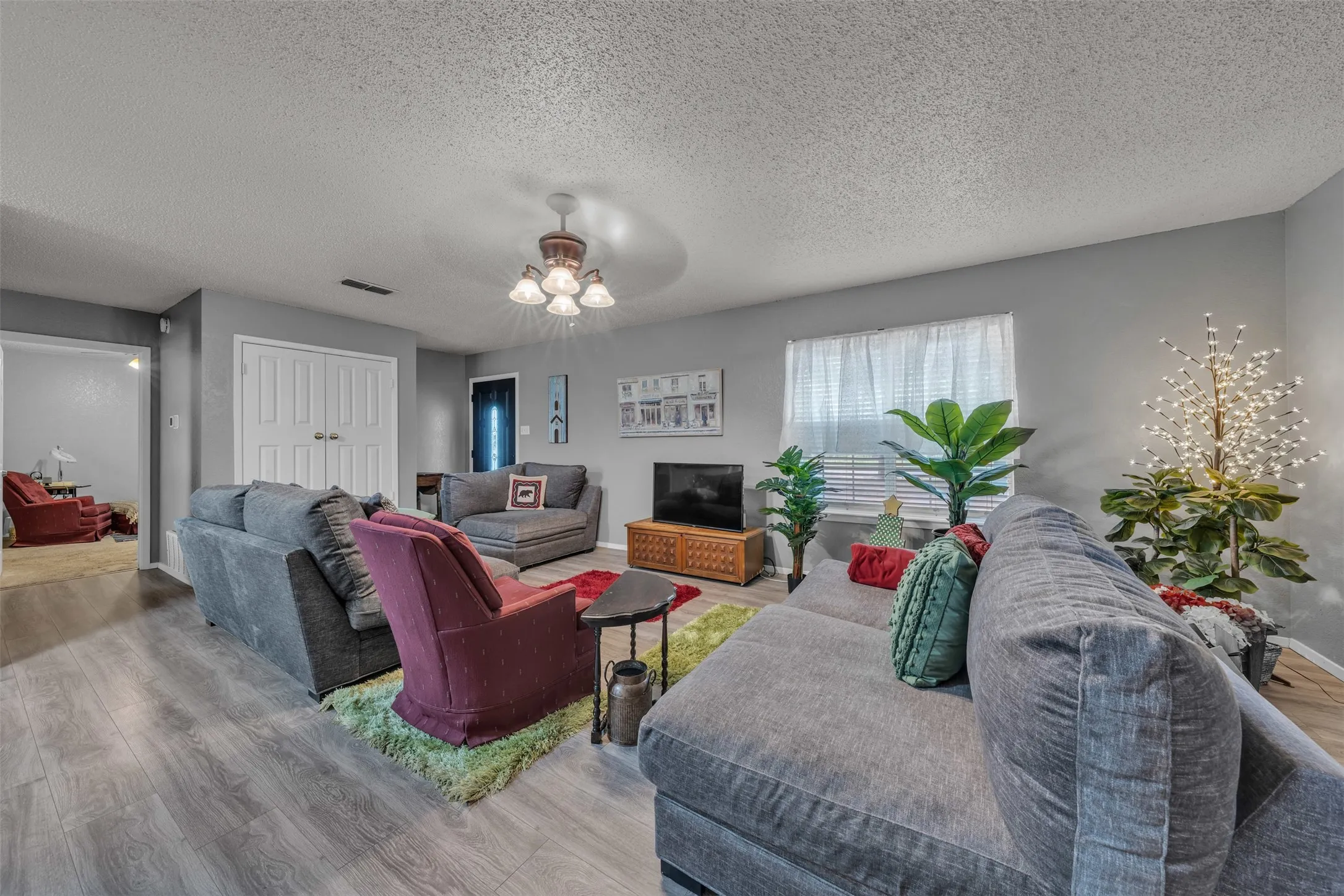 Spacious living area featuring wood-finish flooring, light gray wall tones, a ceiling fan with integrated lighting, and white bi-fold doors-guest quarters