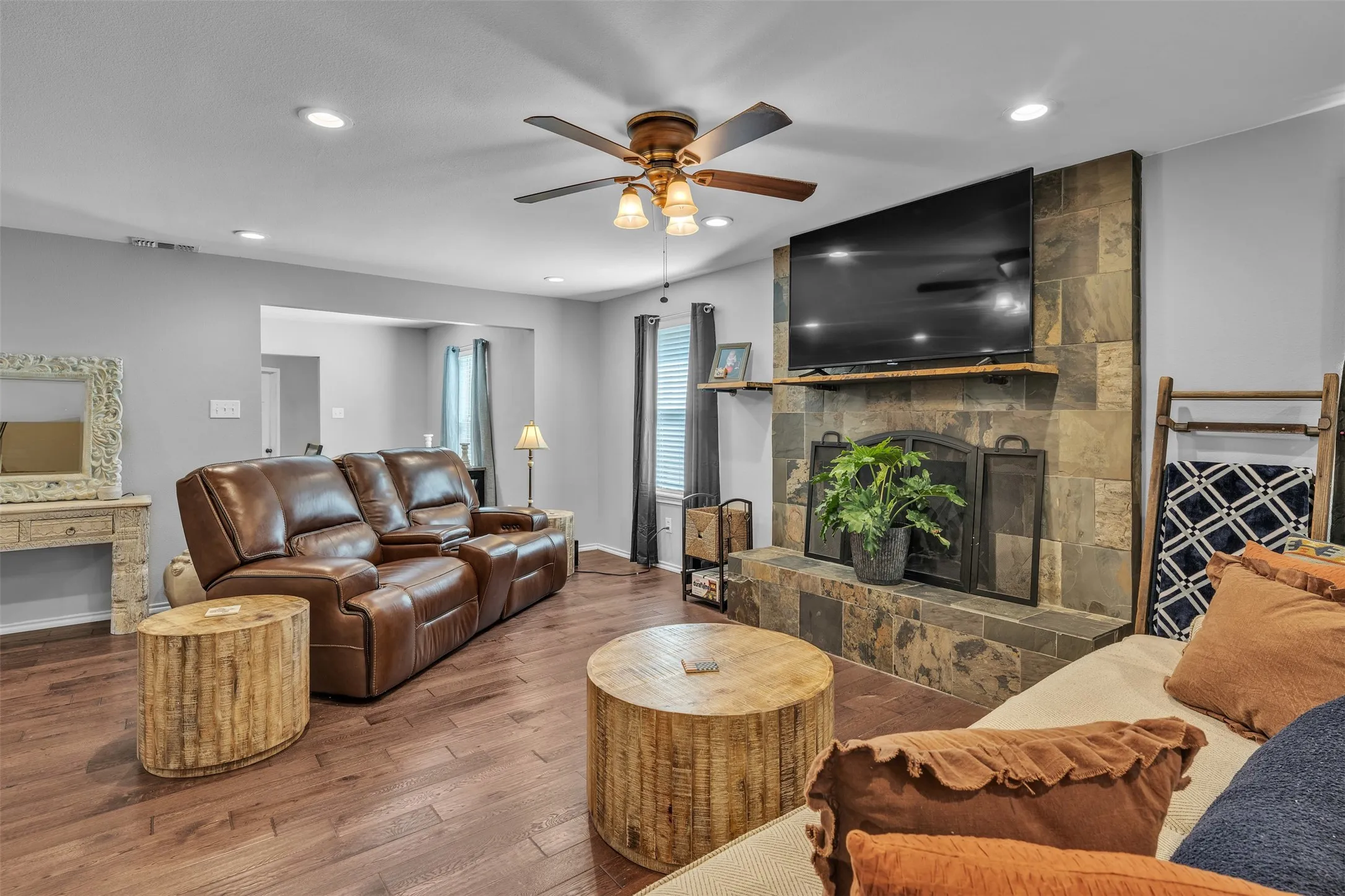Living area featuring wood-finish flooring, a stone-clad fireplace with a built-in mantel, recessed lighting, and a ceiling fan