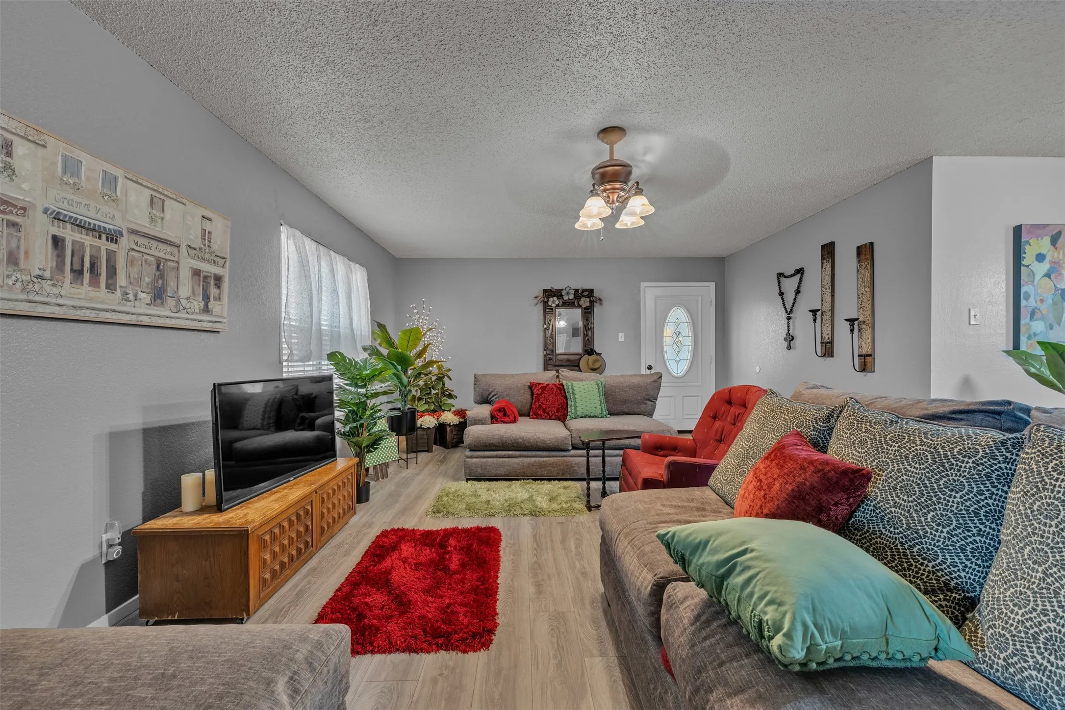 Spacious living area featuring light gray walls, wood-finish flooring, a white entry door with an oval stained-glass insert, and an overhead ceiling fan light fixture-in guest quarters
