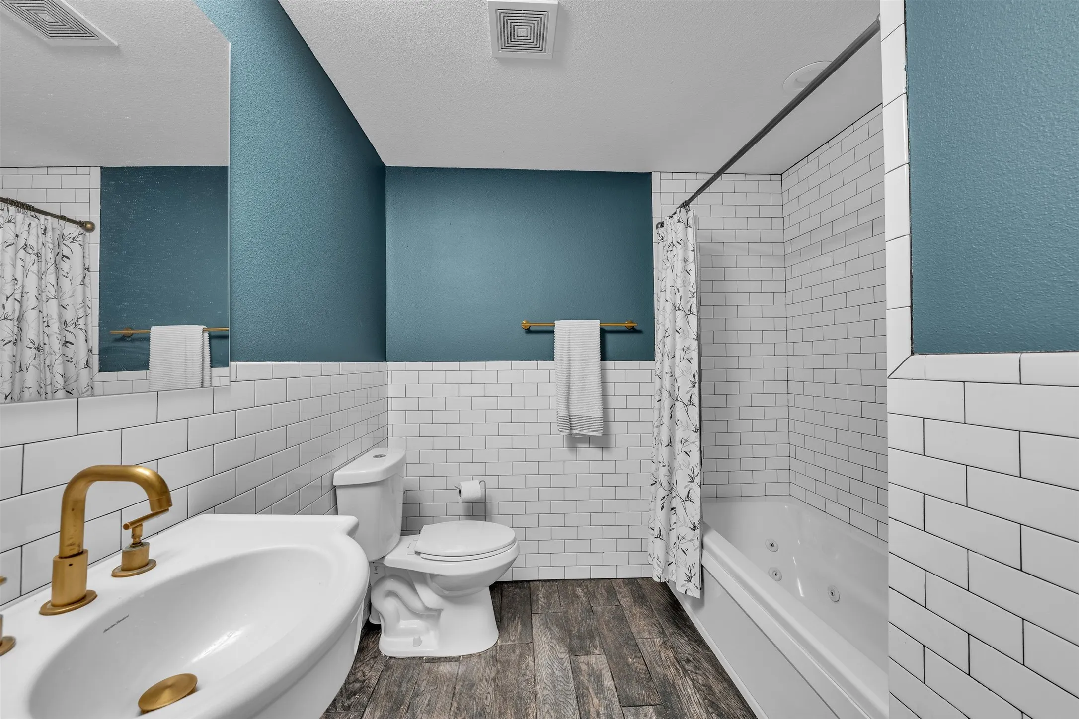 Bathroom featuring a white vanity with a gold-finish faucet, subway tile wainscoting, and a jetted bathtub