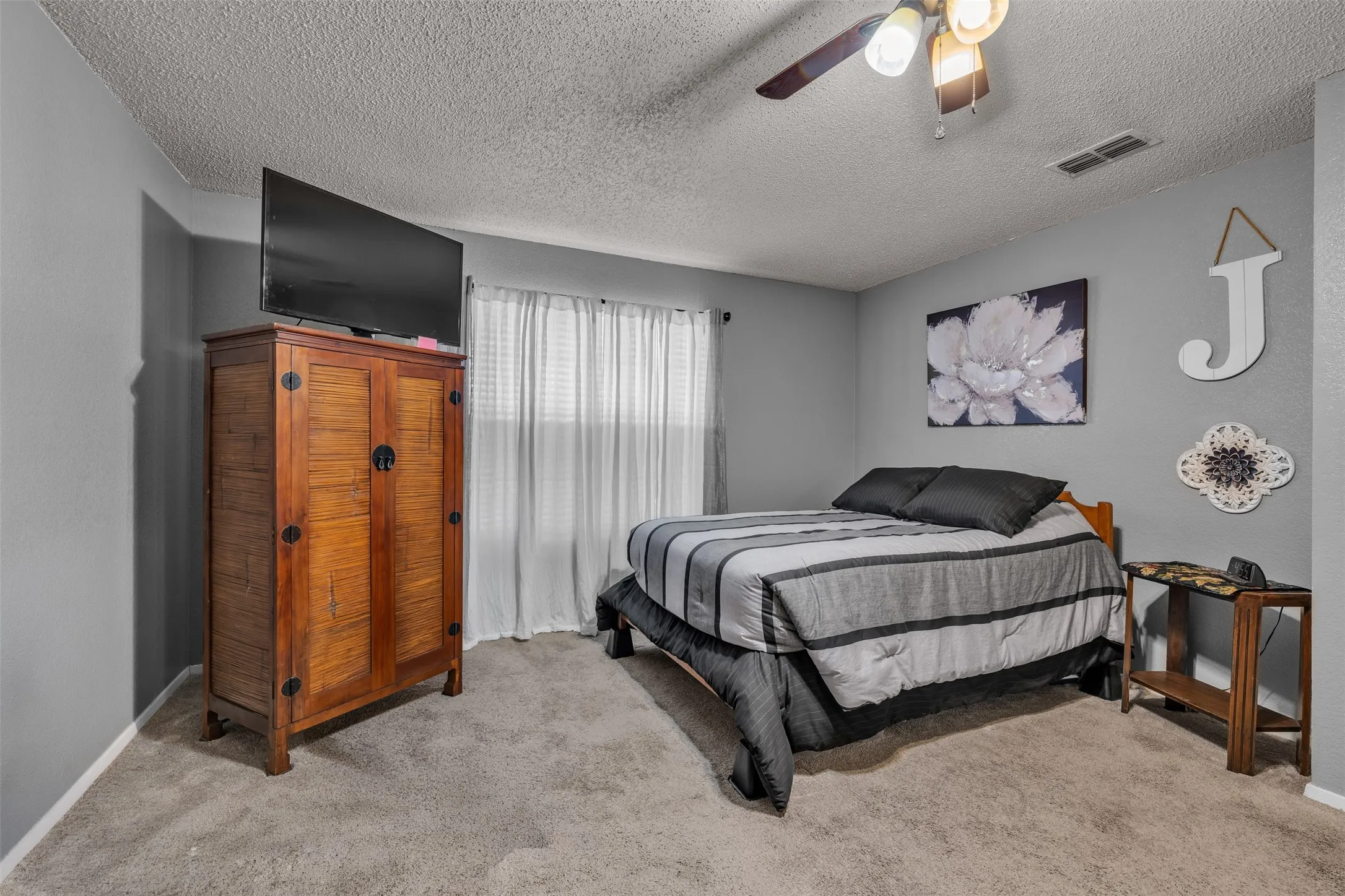 Carpeted room with a ceiling fan light fixture, light gray wall paint, and a window with blinds and sheer curtains