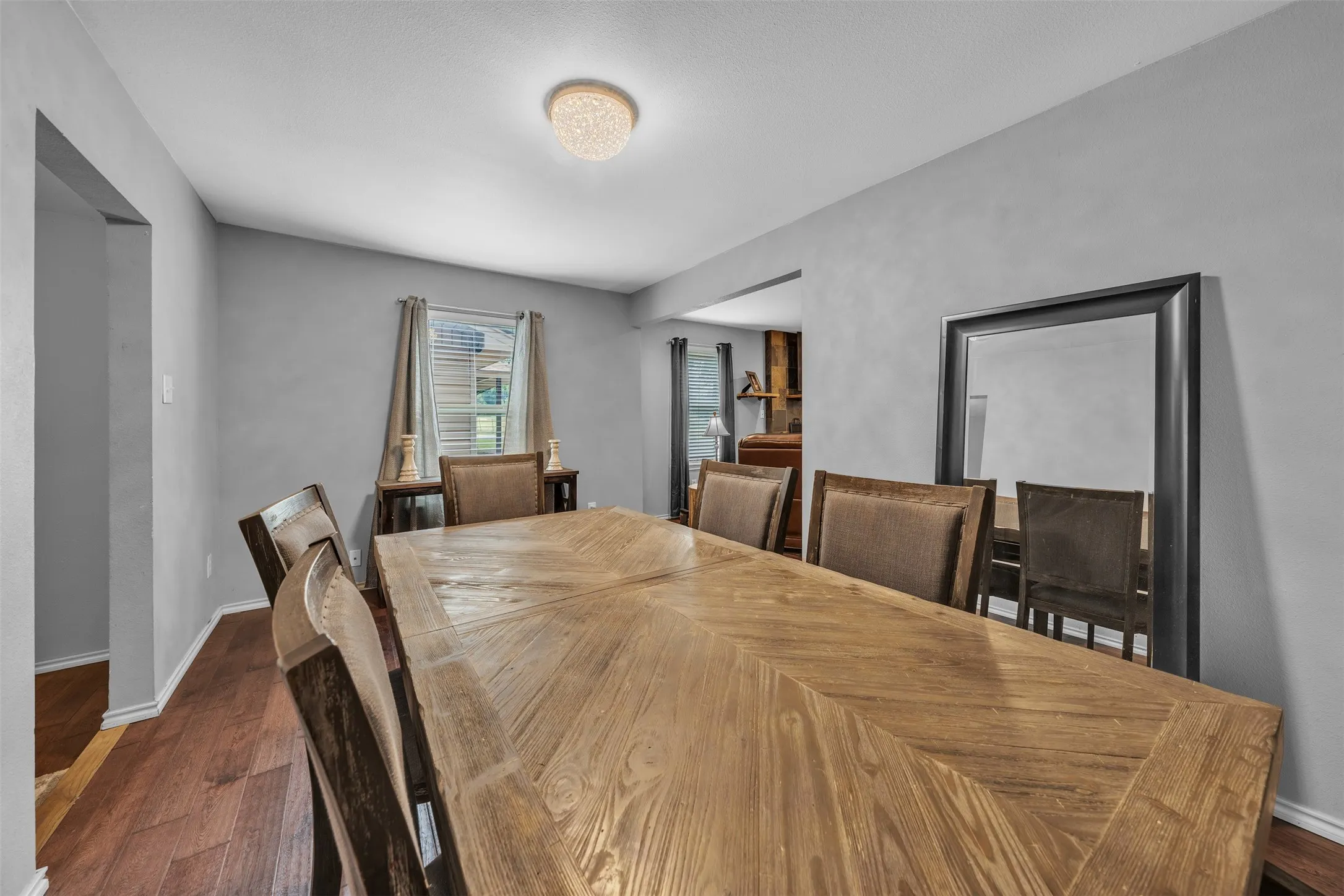 Dining area featuring wood-finish flooring, light gray walls, a window with blinds, and a decorative ceiling light fixture