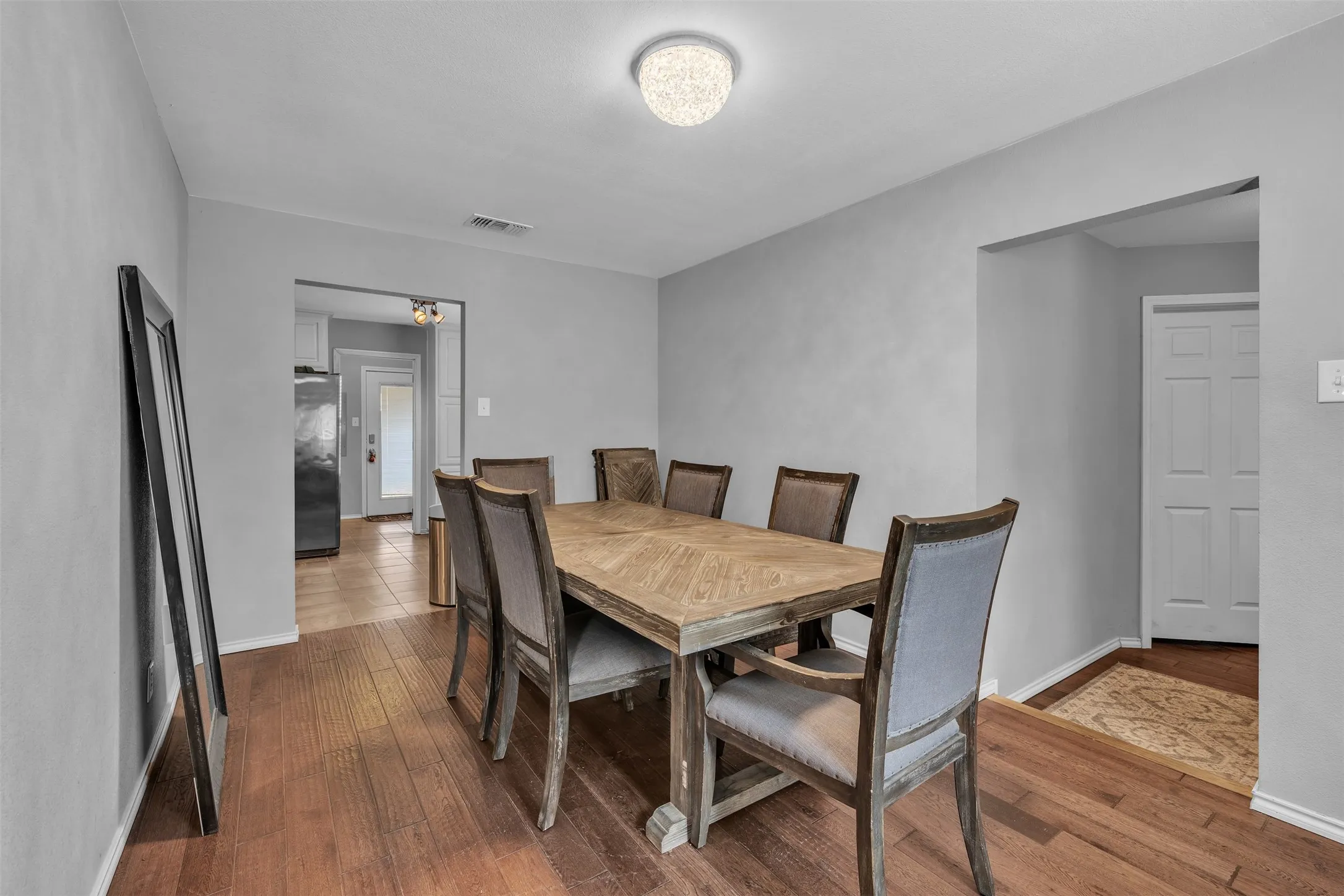 Spacious dining area featuring wood-finish flooring, light gray wall tones, and a ceiling-mounted light fixture
