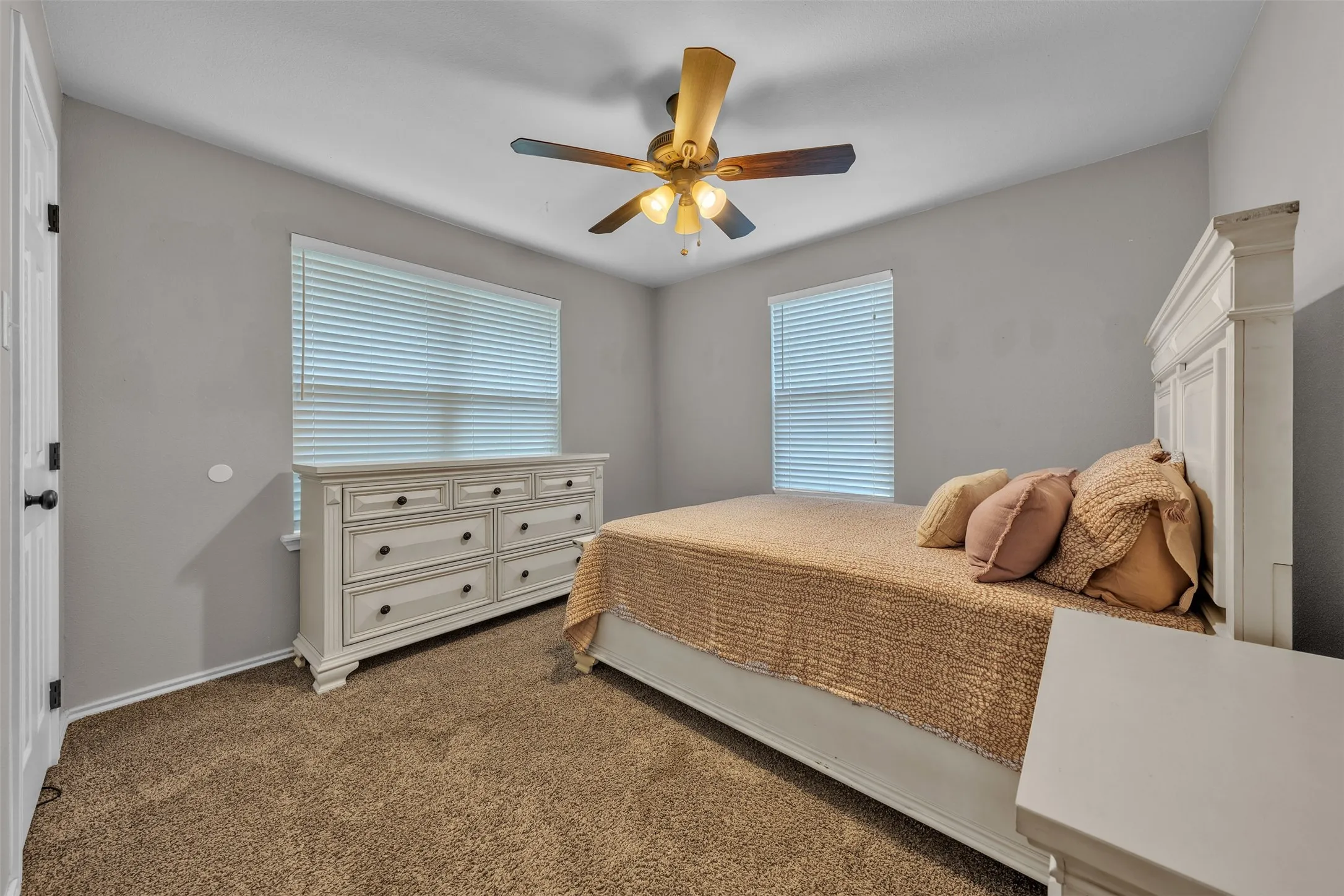 Bedroom featuring textured carpeting, two windows with blinds, a ceiling fan with light fixture, and light gray wall paint