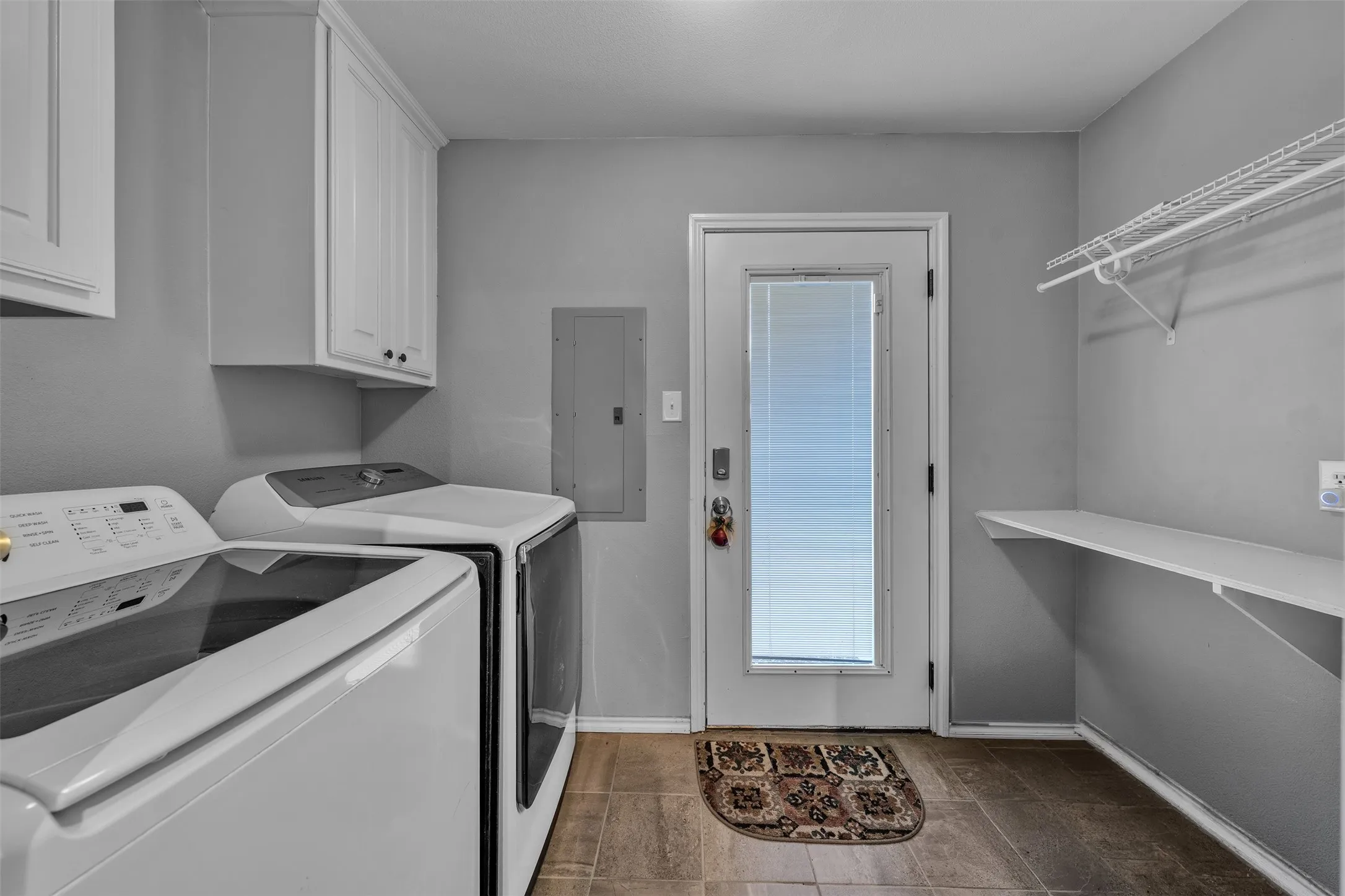 Dedicated utility space featuring tile flooring, white cabinetry, a glass-paneled exterior door with blinds, and built-in shelving