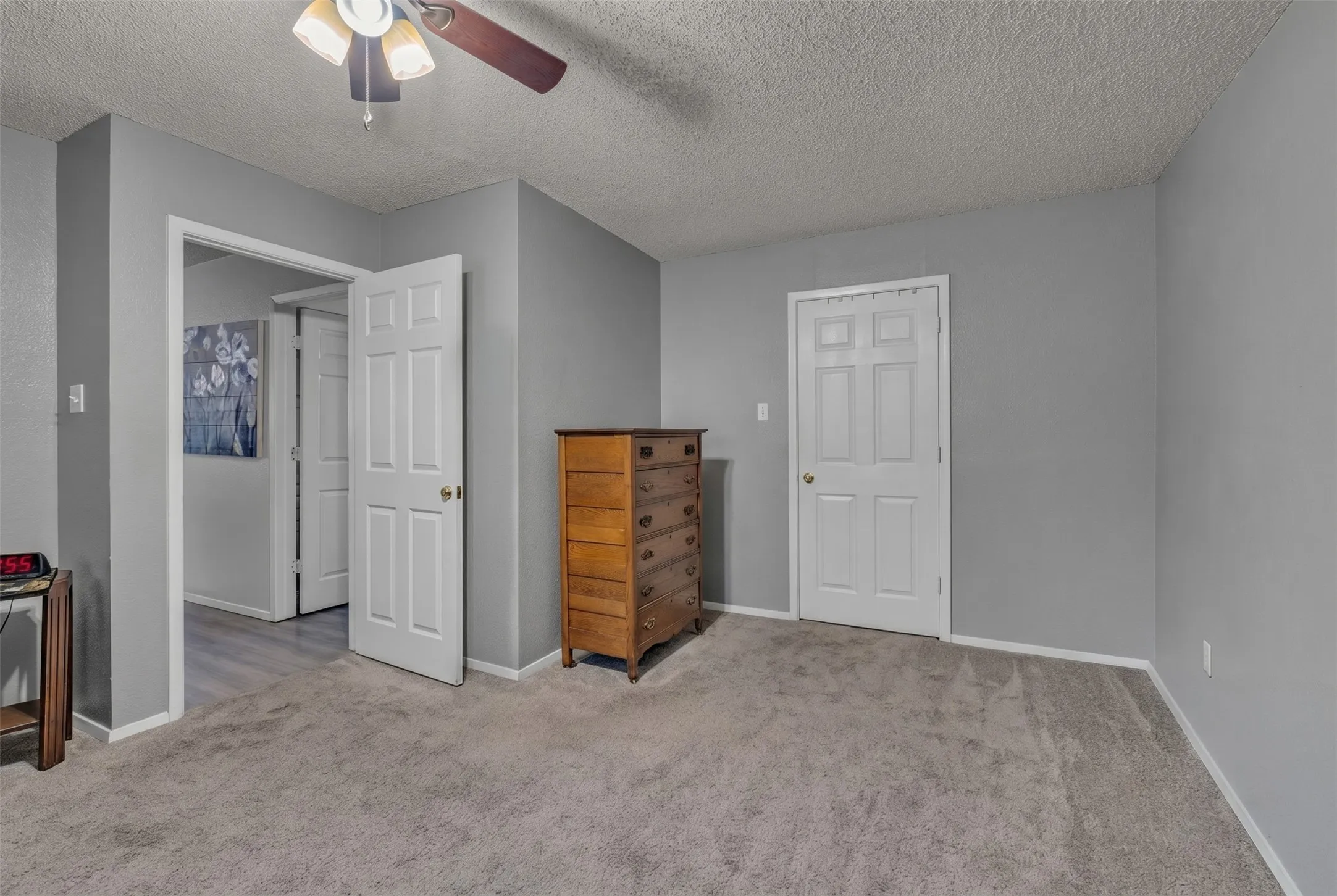 Carpeted bedroom with light gray walls, a white paneled door, and a ceiling fan with integrated lighting