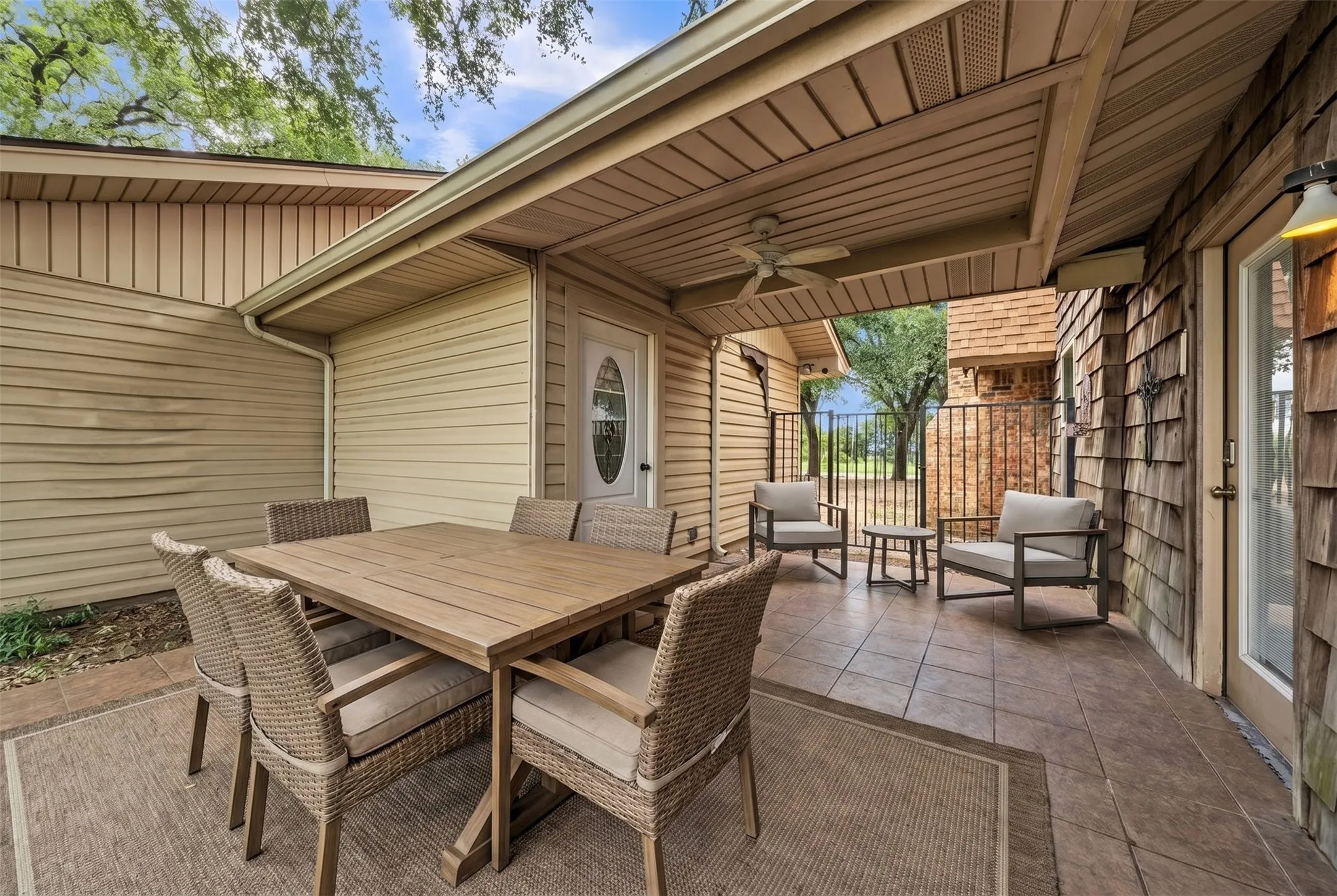 Covered patio area featuring a ceiling fan, tiled flooring, and a door with an oval glass insert in between main home and guest quarters