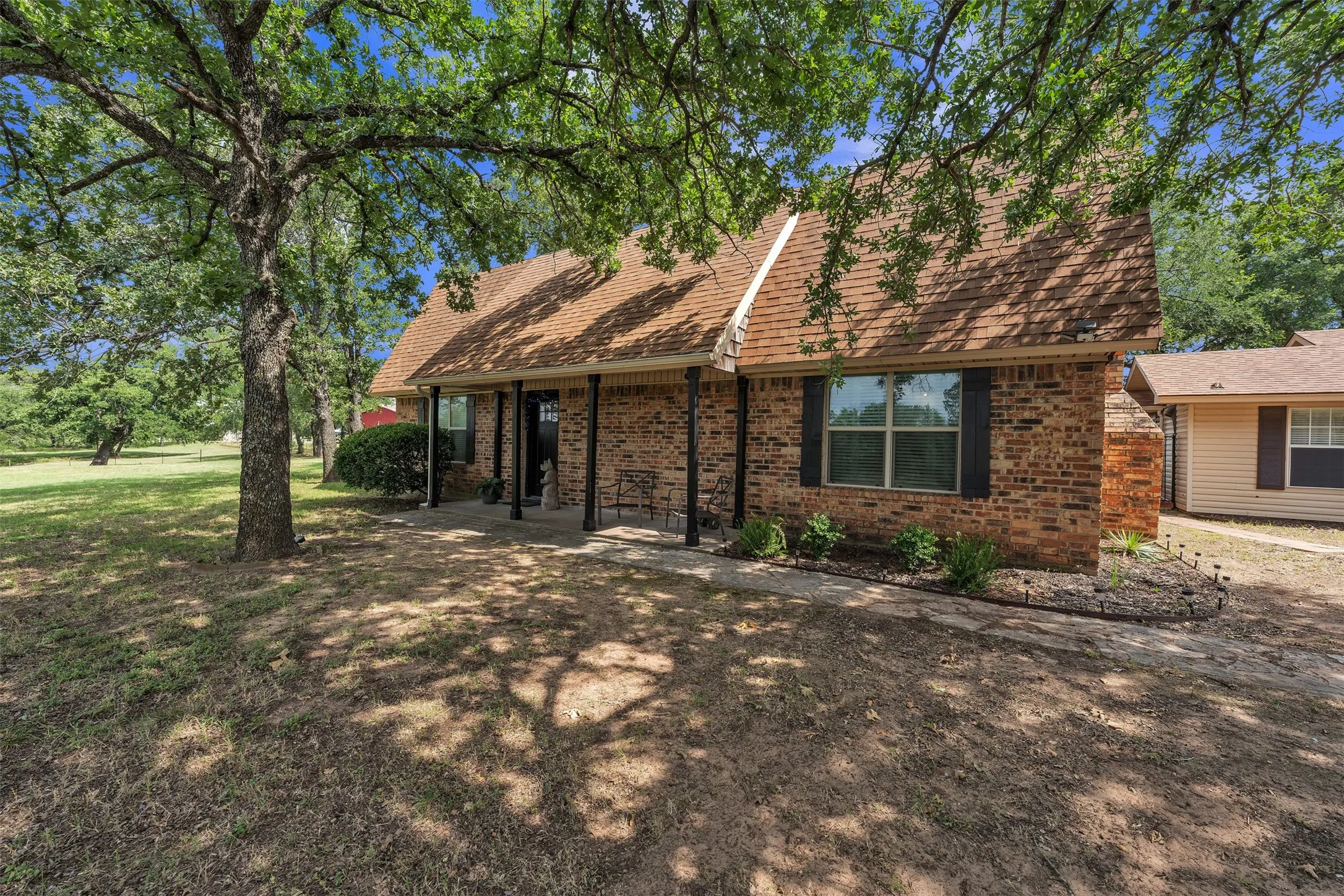 Brick exterior residence with a brown shingle roof and a covered front porch featuring black support columns