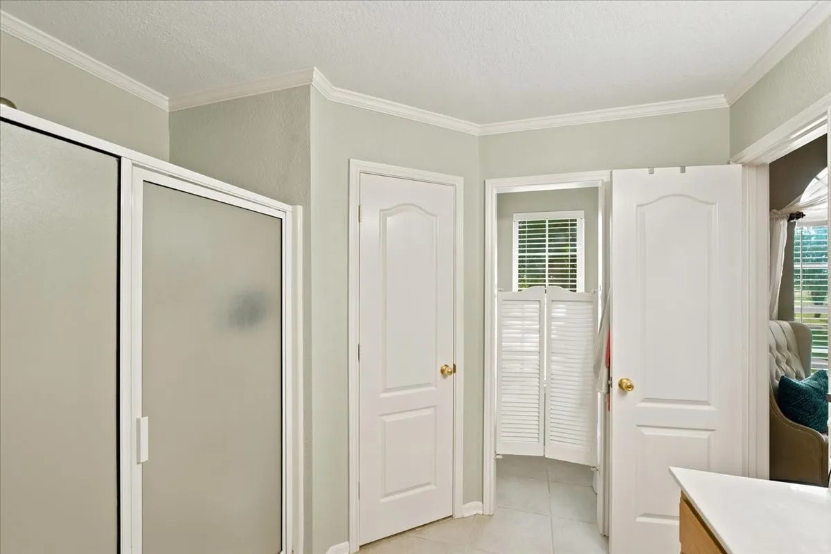 Bathroom featuring a frosted glass shower enclosure, white interior doors with brass hardware, tile flooring, and crown molding